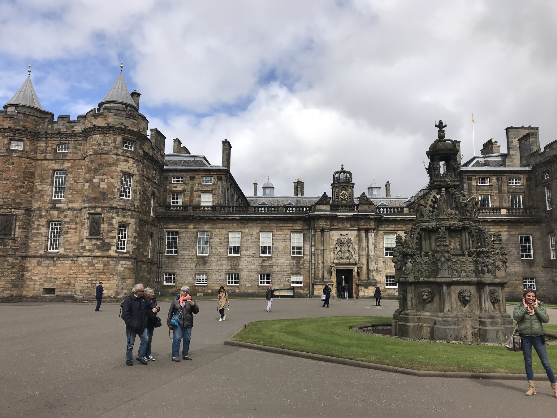 Visitors crossing the forecourt of the Palace of Holyroodhouse beneath a cloudy sky