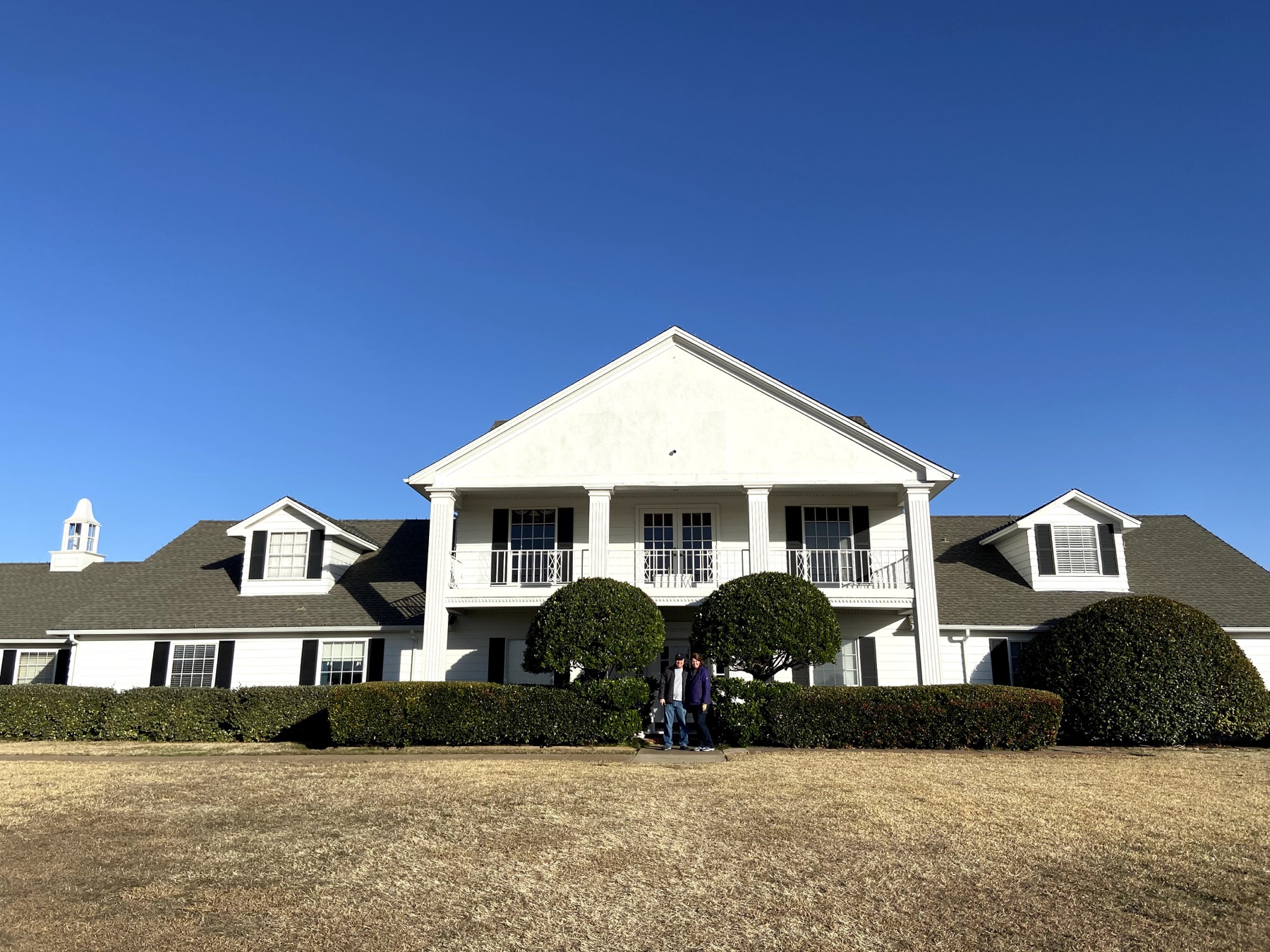 Angela and Brian standing in front of the white Ewing Mansion at Southfork Ranch
