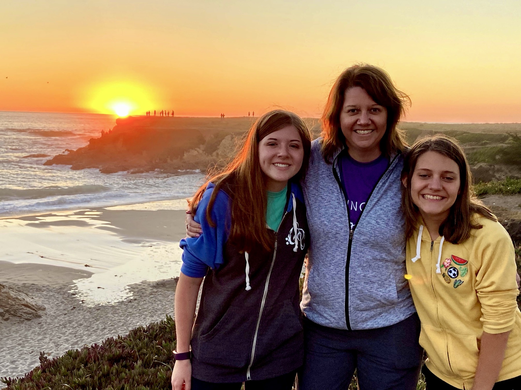 Angela and her daughters standing in front of a Pacific Ocean sunset in Fort Bragg