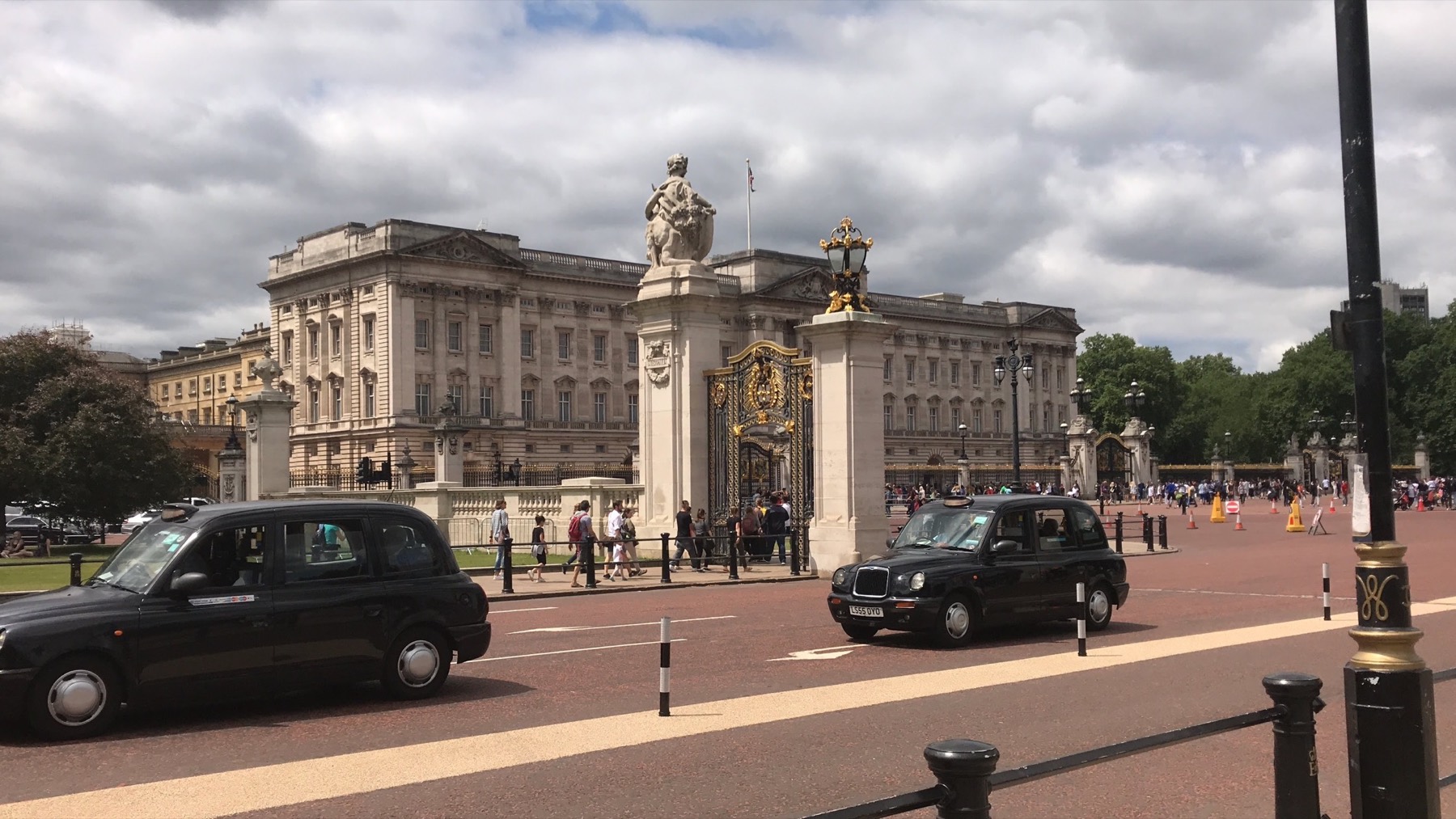 Buckingham Palace and the Victoria Memorial viewed across a crowd beneath dramatic clouds
