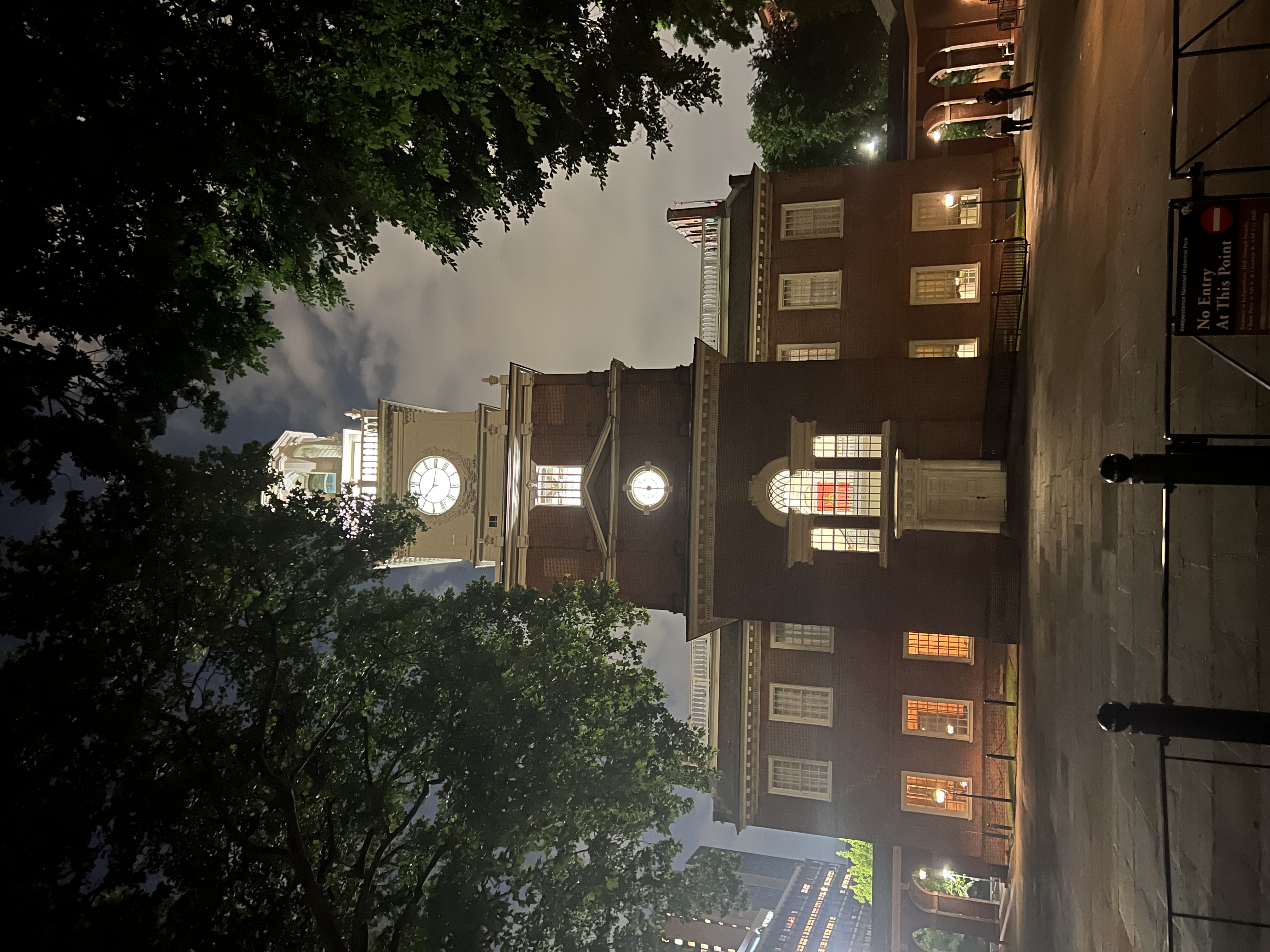 Illuminated clock tower of Independence Hall seen through trees at night