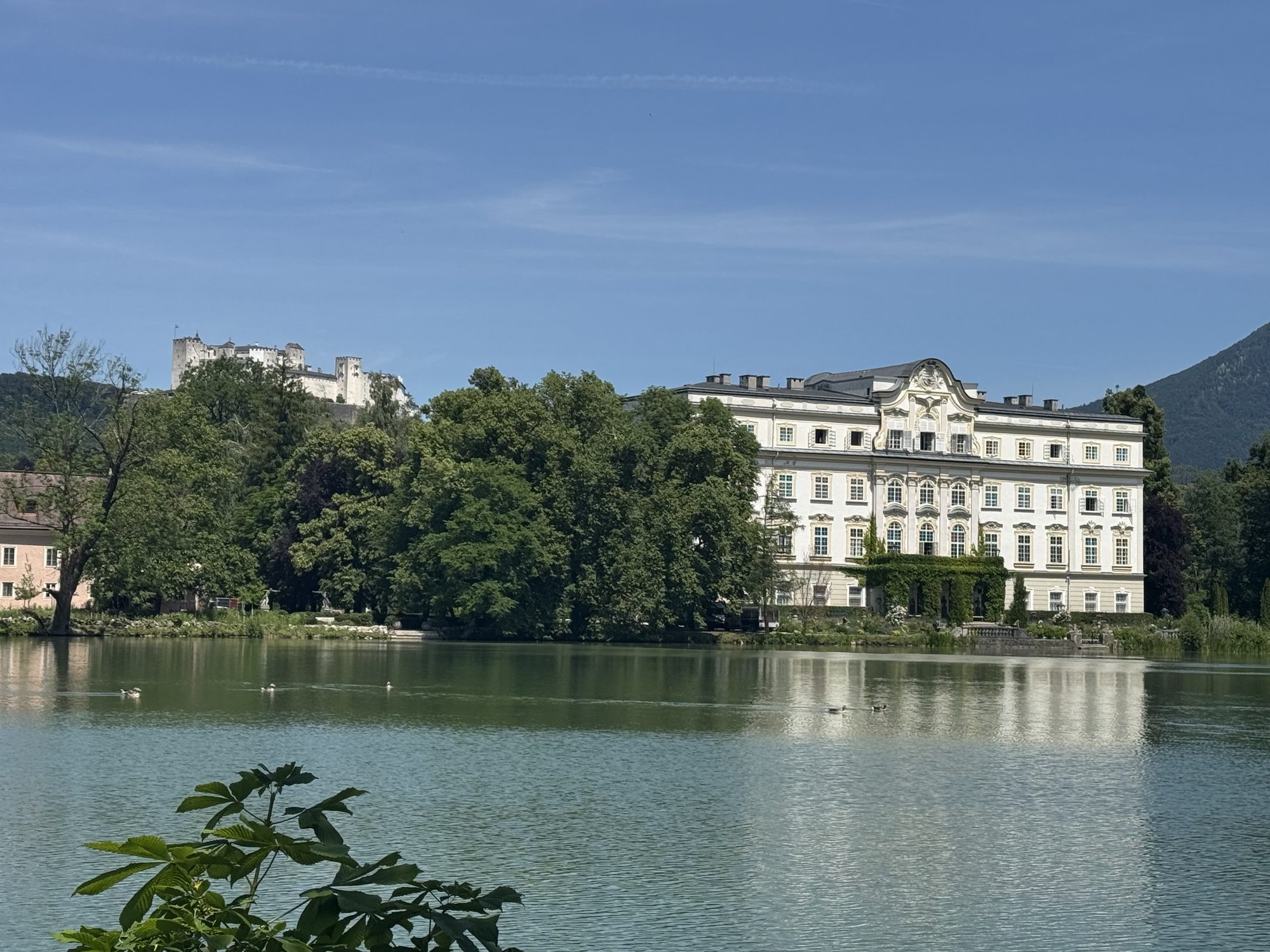 Leopoldskron Palace on the edge of its lake with Hohensalzburg Fortress on the hill behind it
