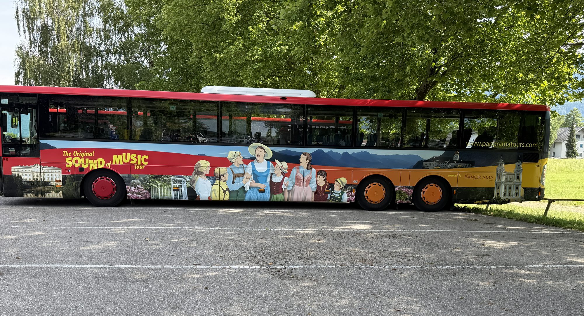 A colorful Original Sound of Music Tour bus parked beneath green trees