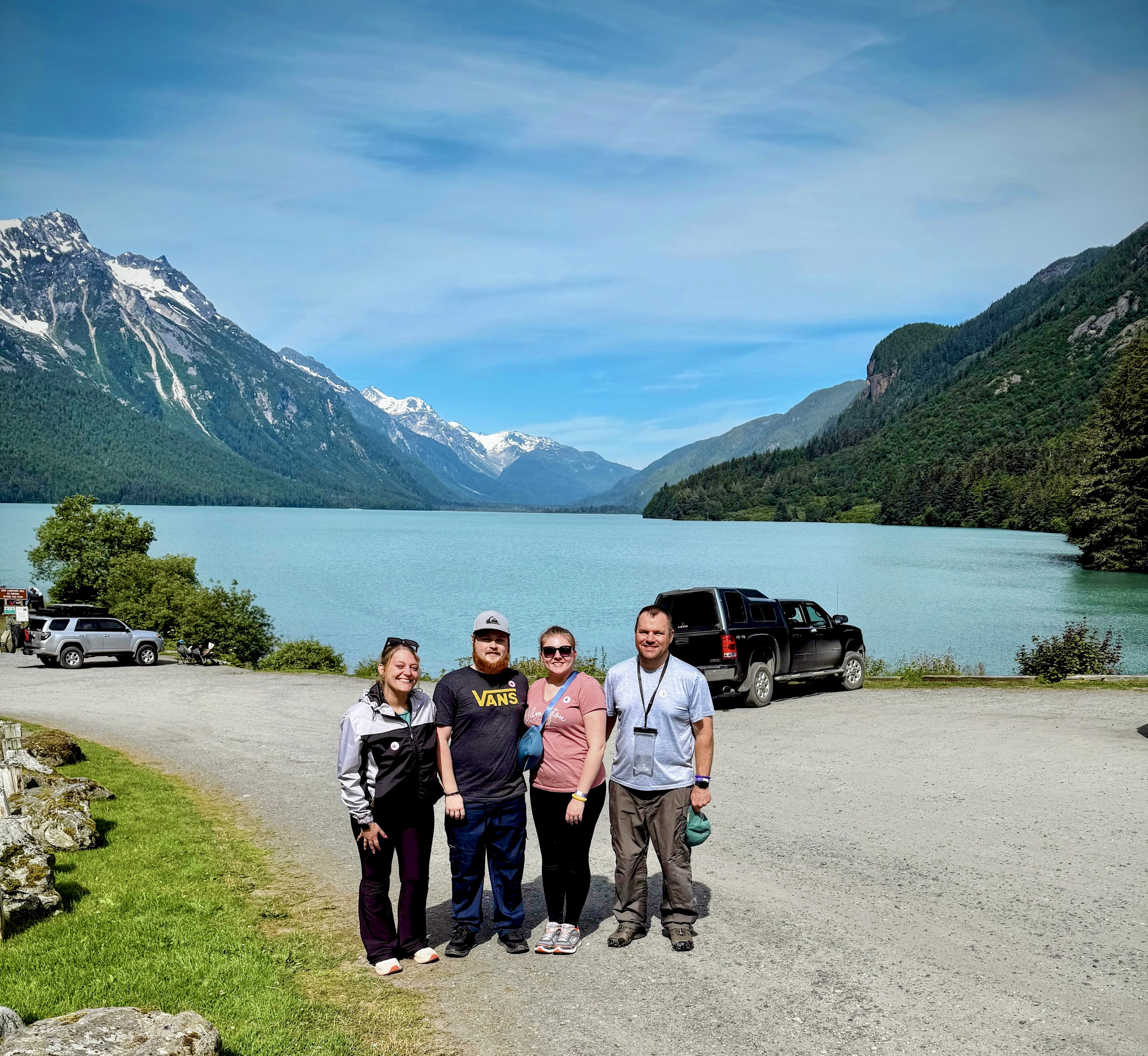 Four members of the group standing beside Chilkoot Lake with snowy mountains beyond