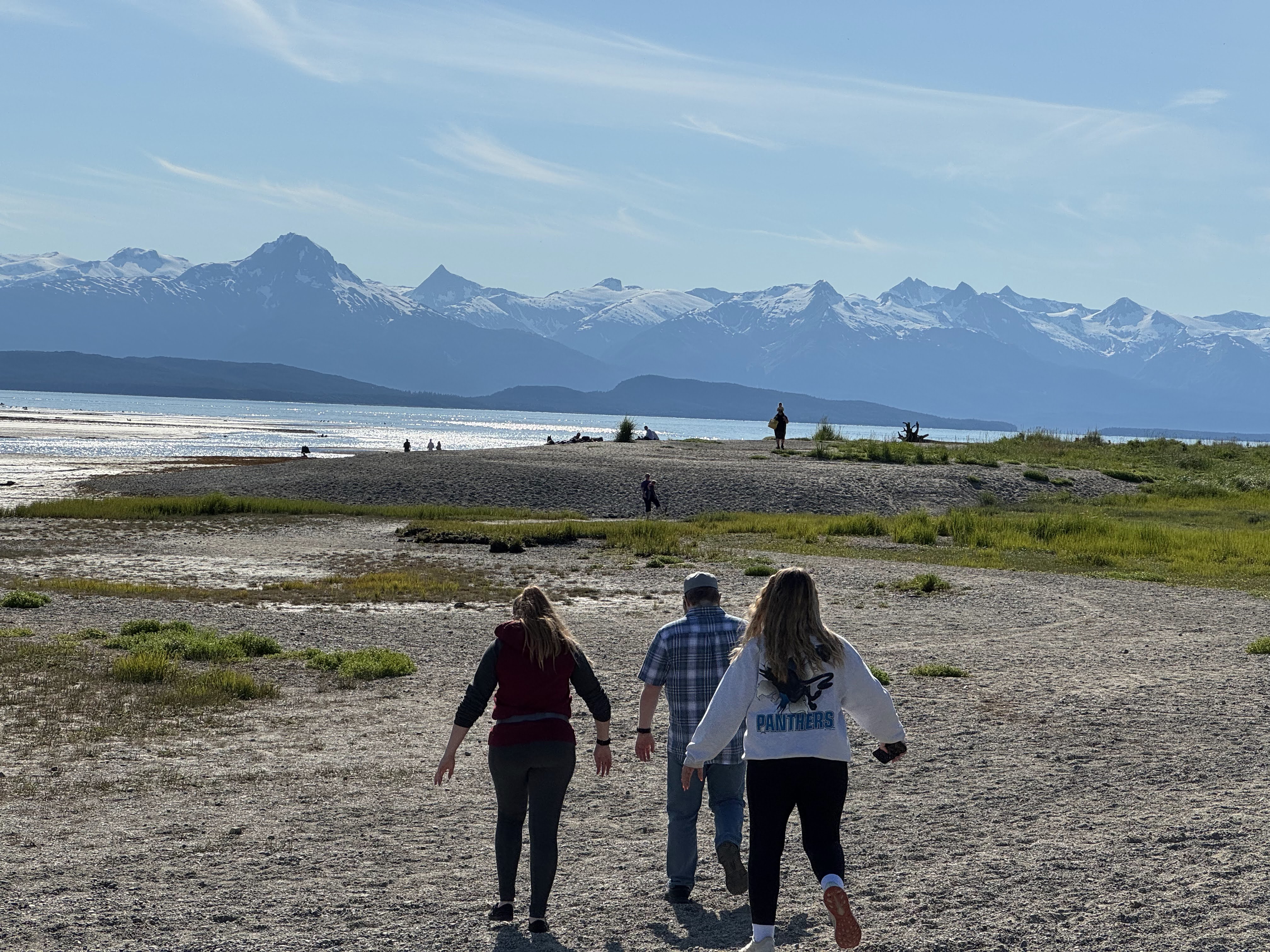 Family members walking across the broad low-tide shoreline at Eagle Beach with snow-covered mountains across the water