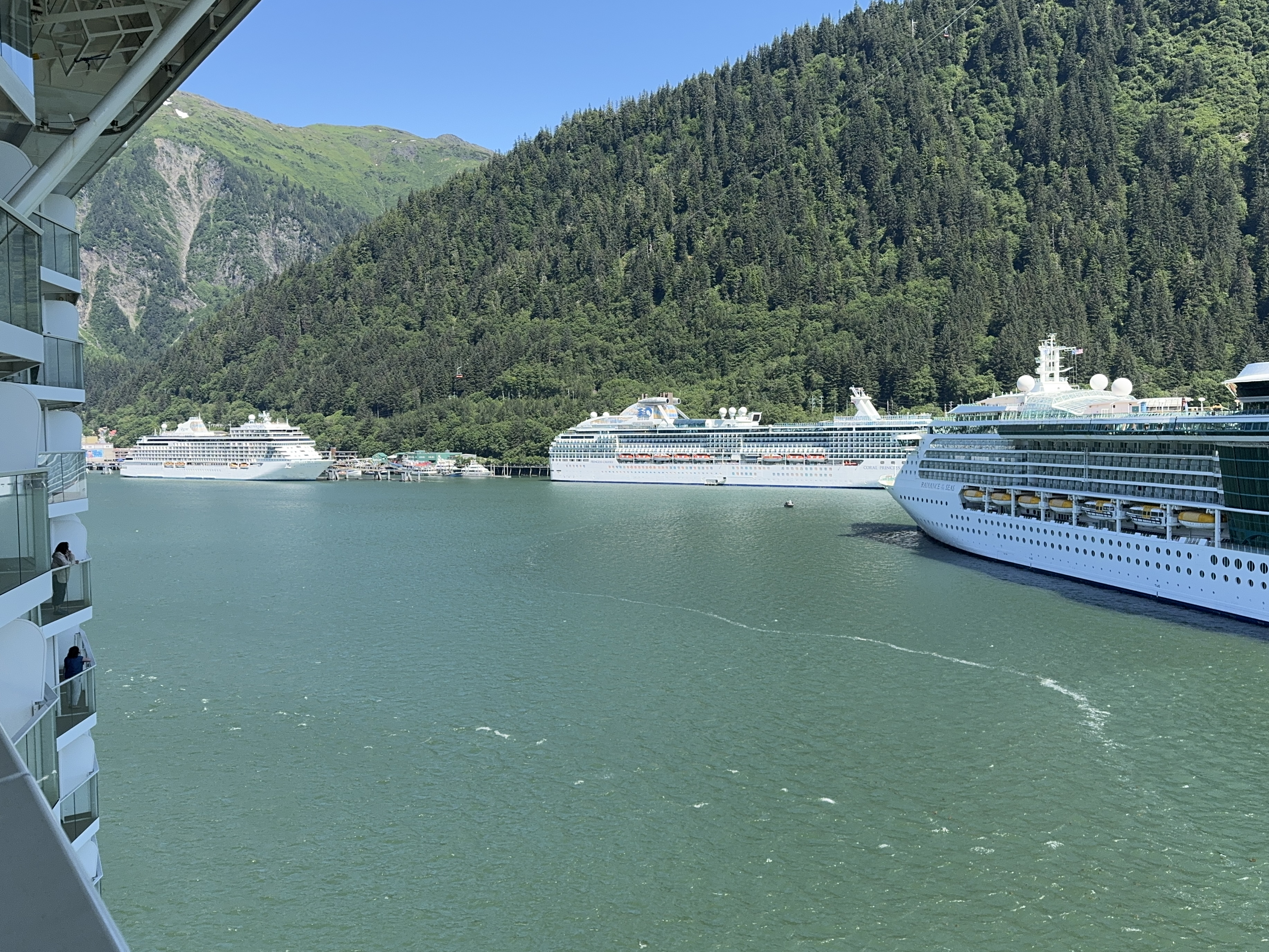 Several large cruise ships docked in Juneau beneath a steep forested mountainside