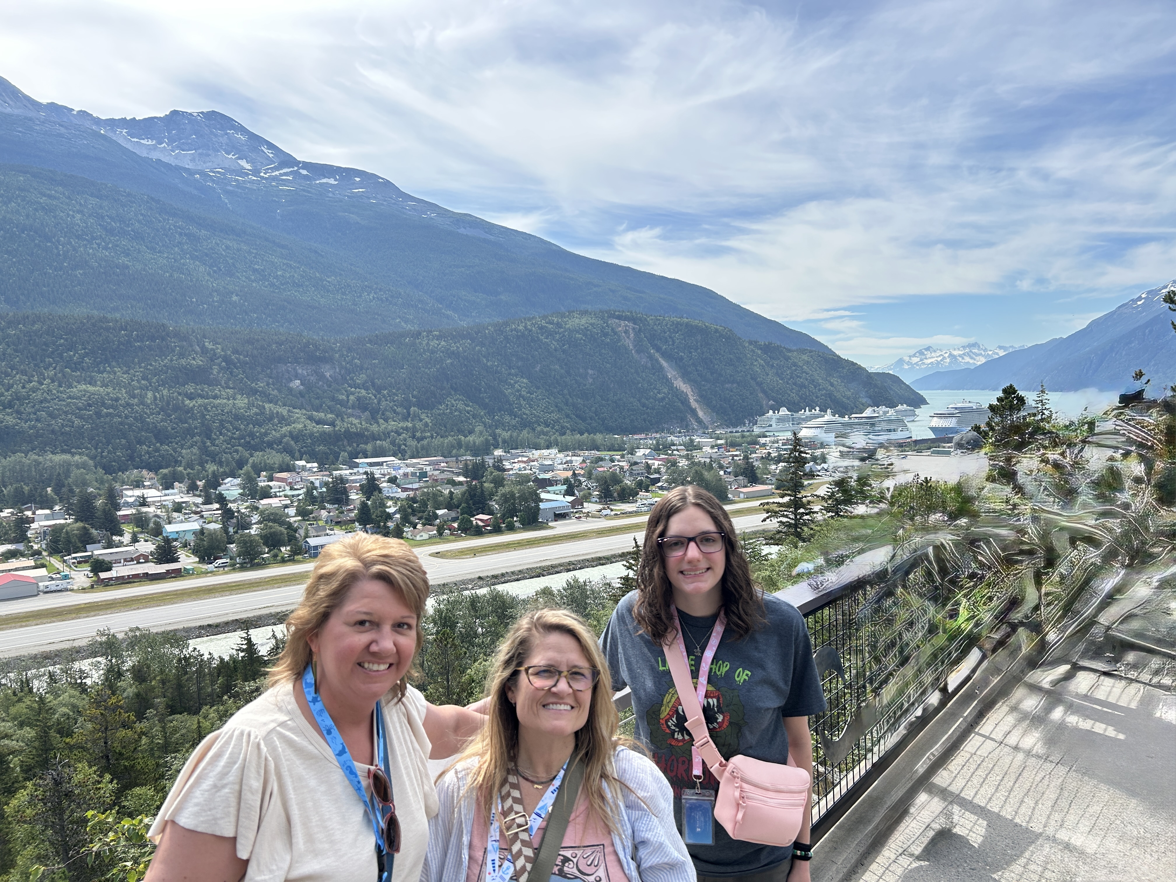 Angela, Beth, and Sidney smiling at an overlook above Skagway with cruise ships in the harbor below