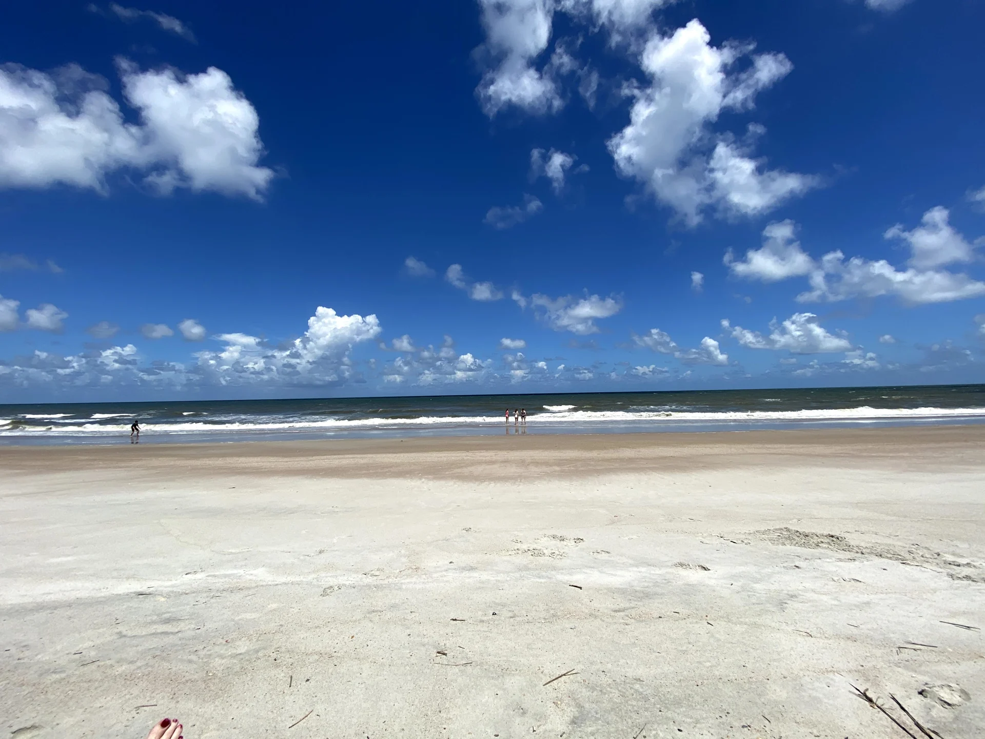 Broad stretch of pale sand and Atlantic surf beneath a blue sky with white clouds on Amelia Island