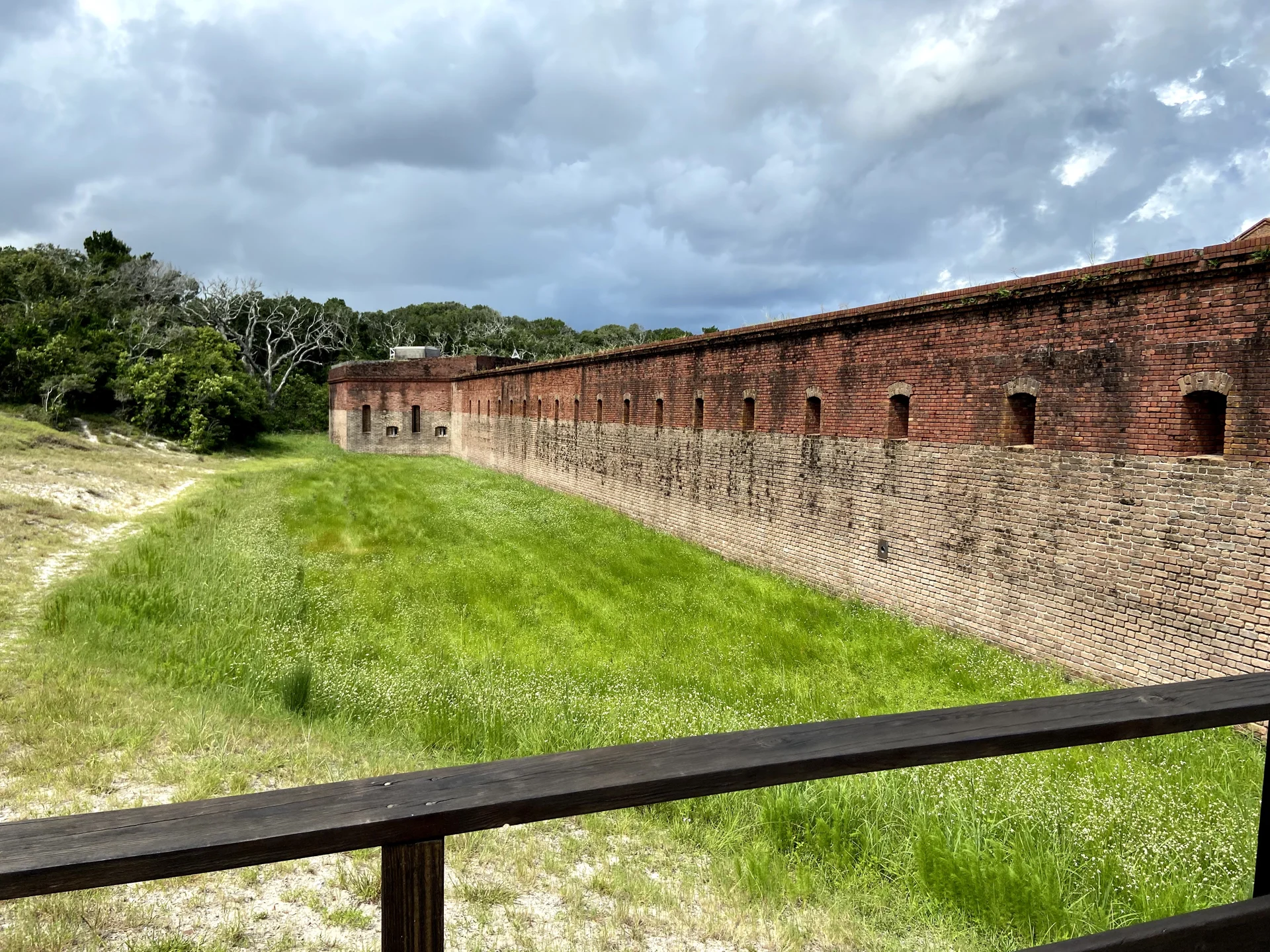 Long brick walls of Fort Clinch above a grassy area, viewed from behind a wooden railing