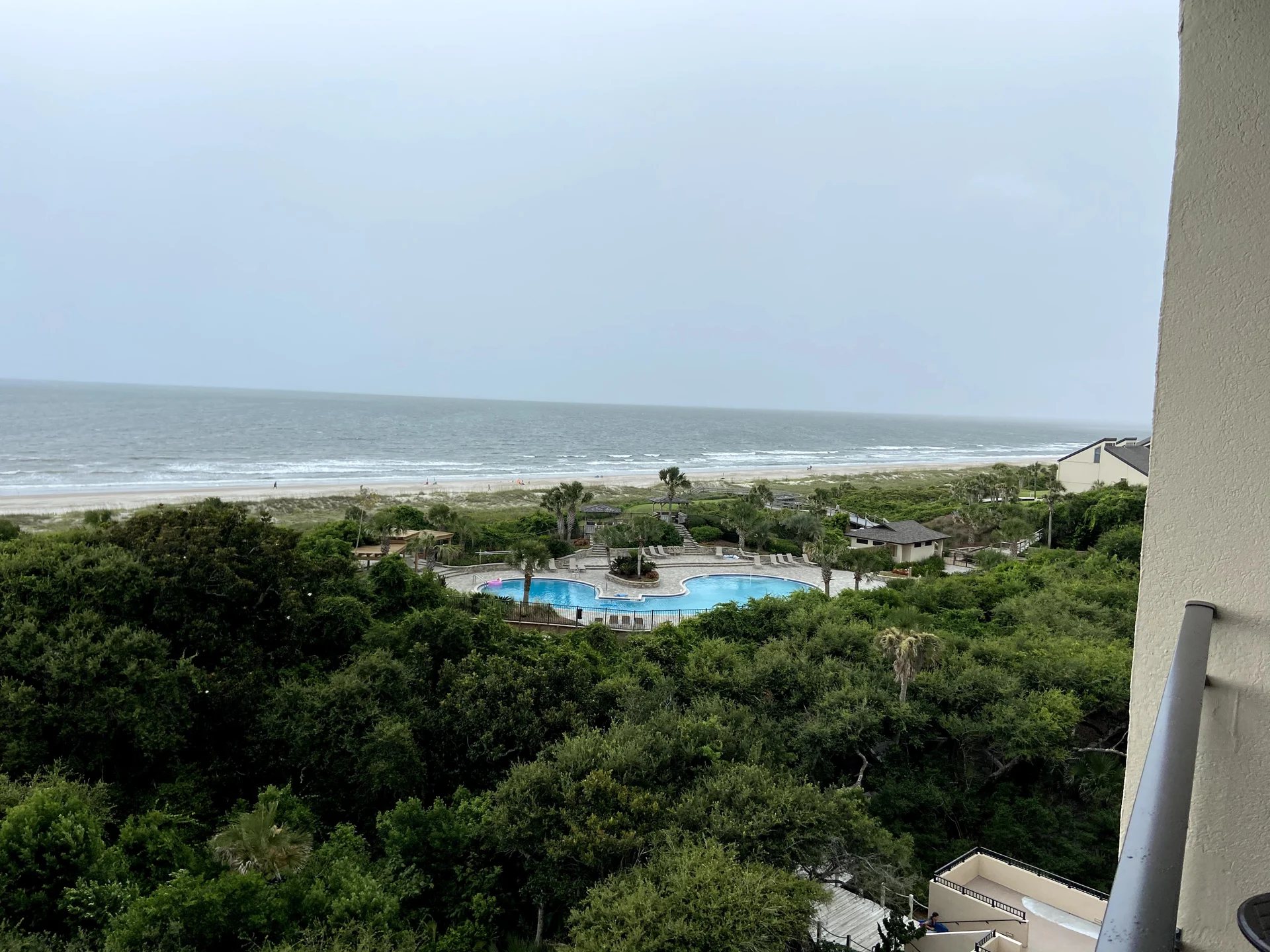 View from our rental toward a swimming pool, coastal greenery, and the Atlantic Ocean under cloudy skies