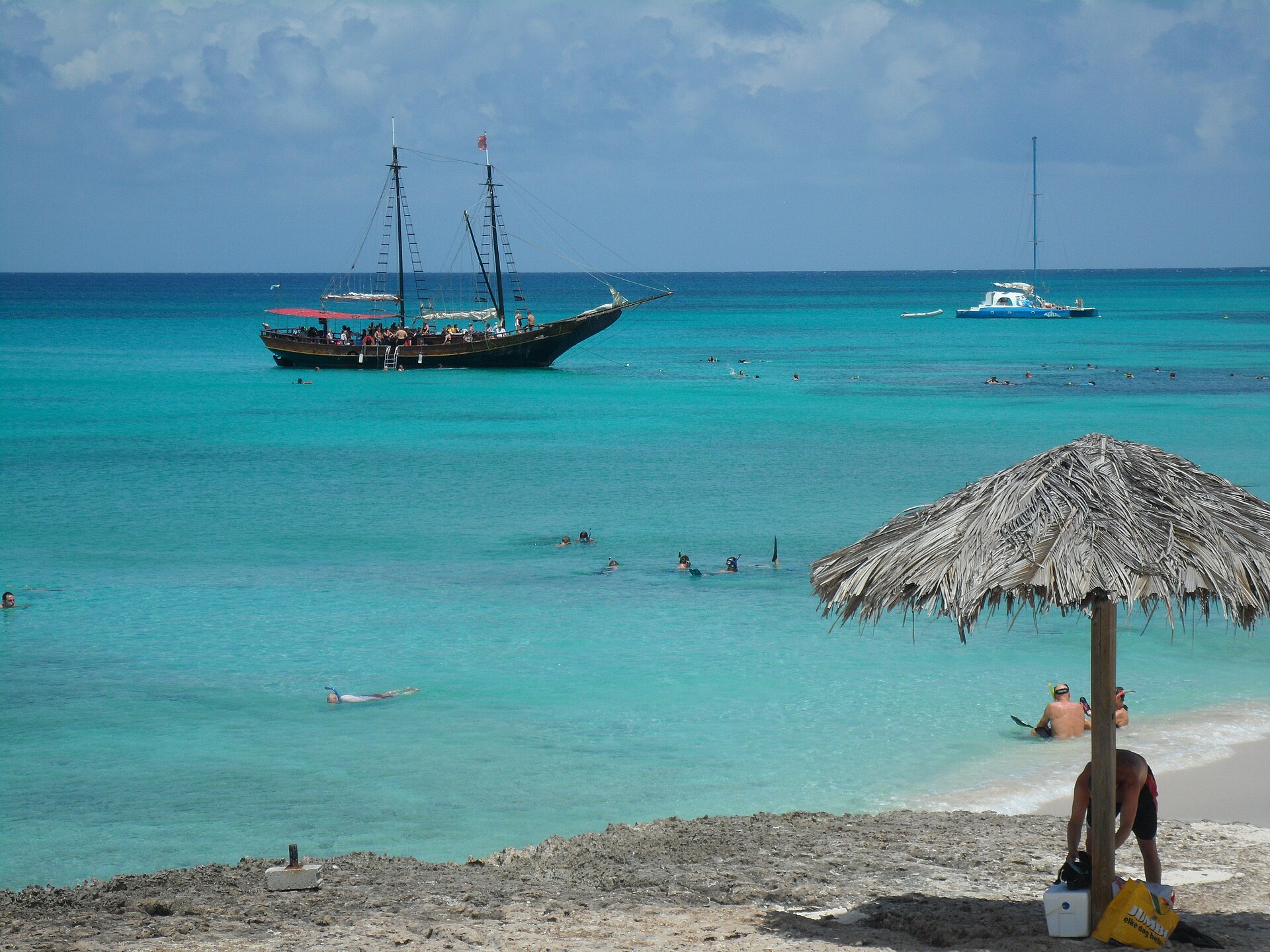 Snorkelers in clear turquoise water beside a sailing schooner in Aruba