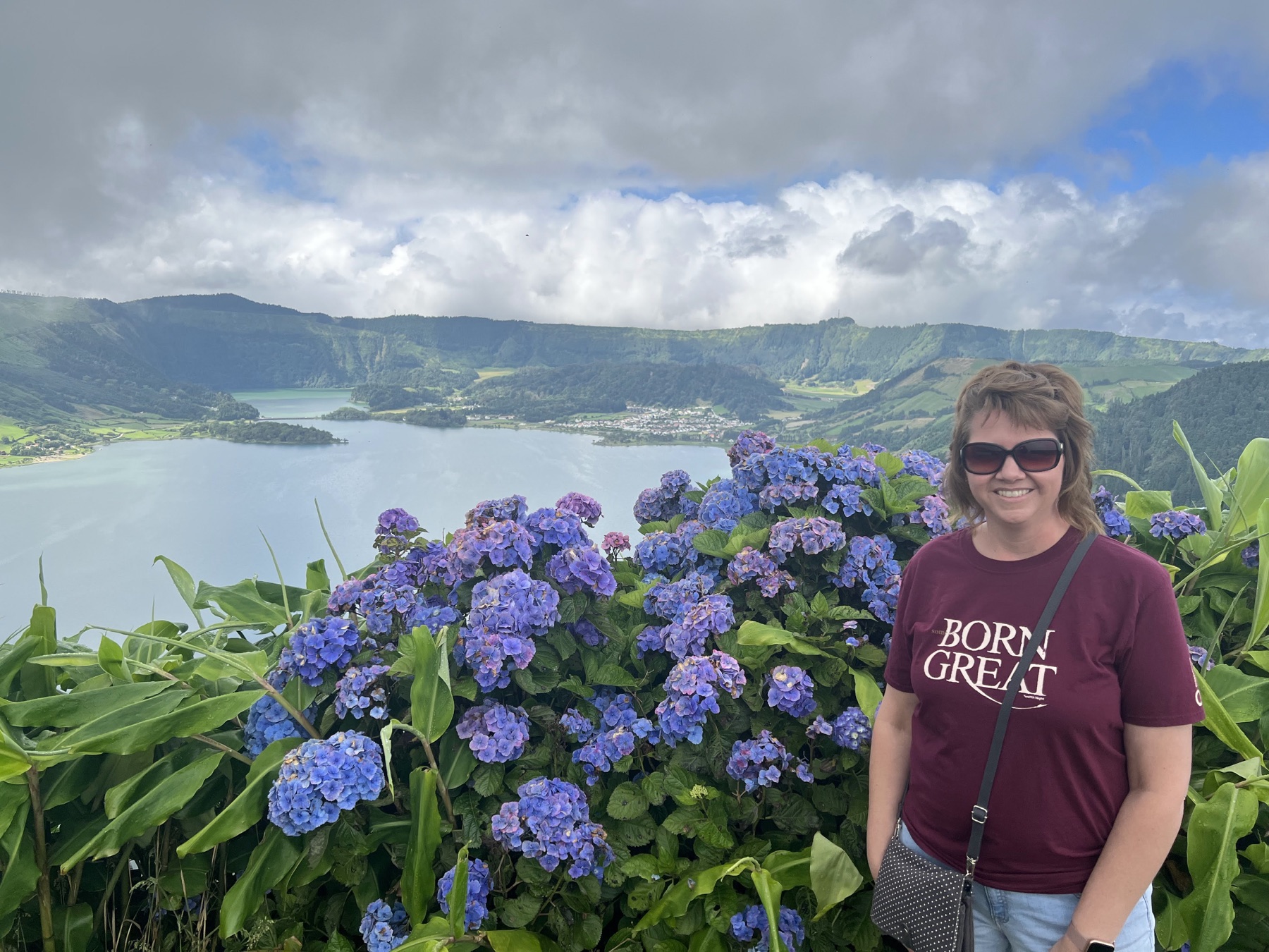 Angela standing beside blue hydrangeas at a viewpoint above the Sete Cidades crater lakes on São Miguel