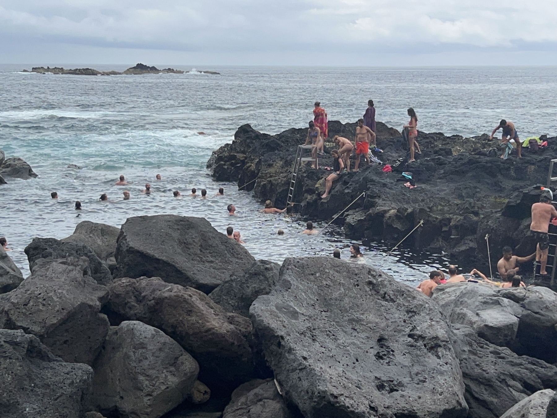 Swimmers in a natural ocean pool surrounded by dark volcanic rocks at Ponta da Ferraria