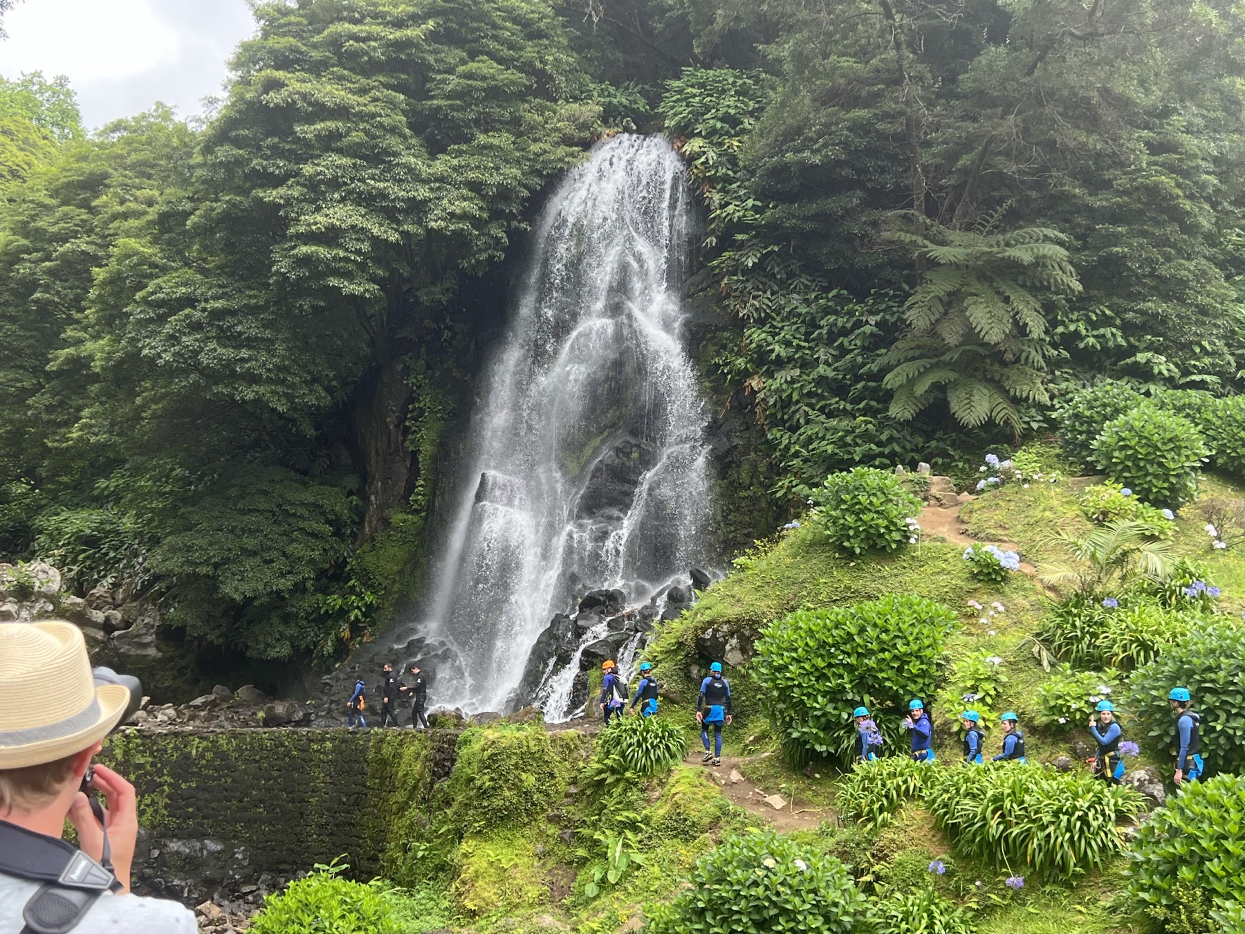 Tall waterfall spilling through dense green forest as visitors stand nearby