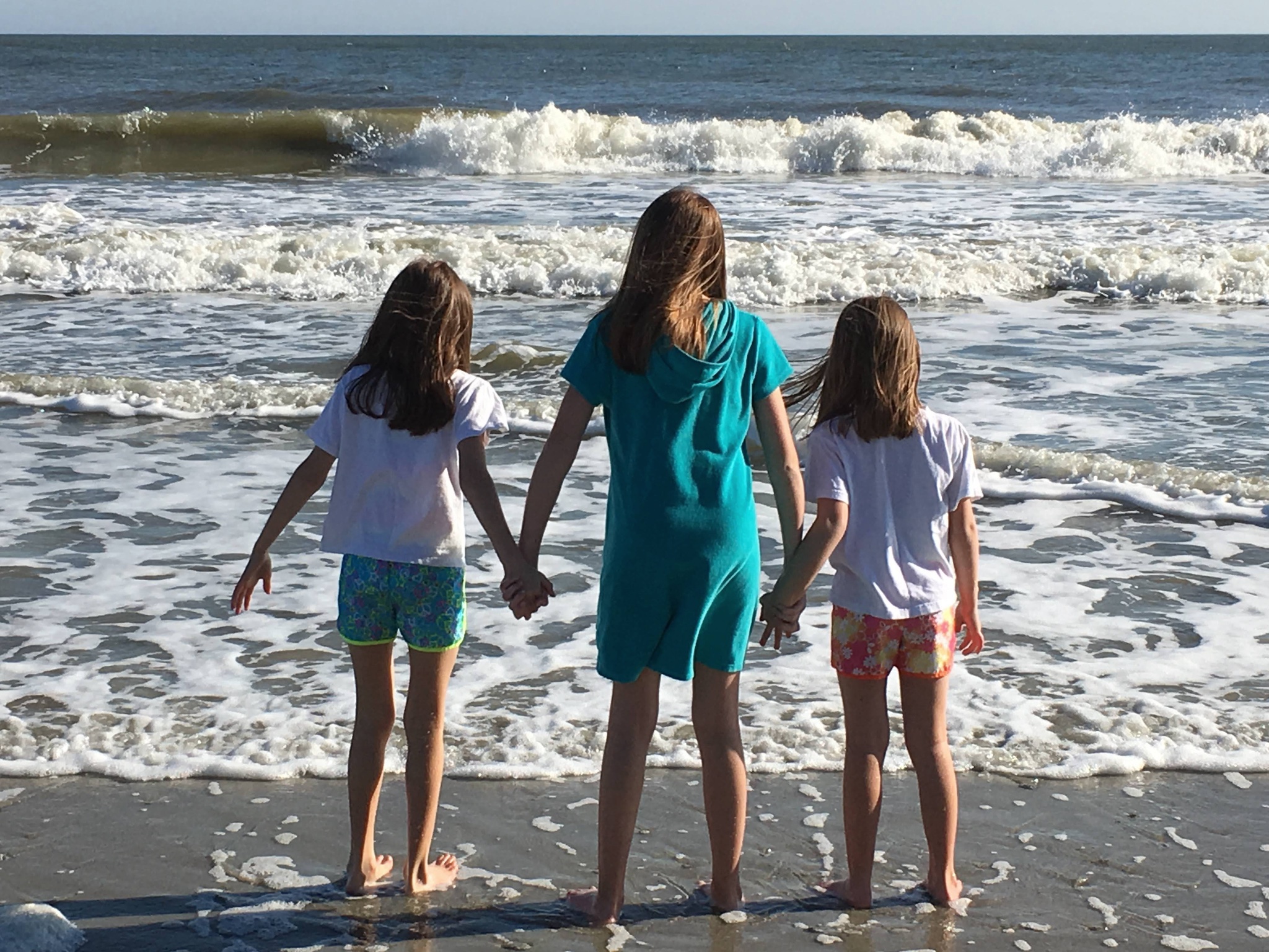 Angie’s three daughters holding hands at the edge of the ocean in Myrtle Beach, South Carolina