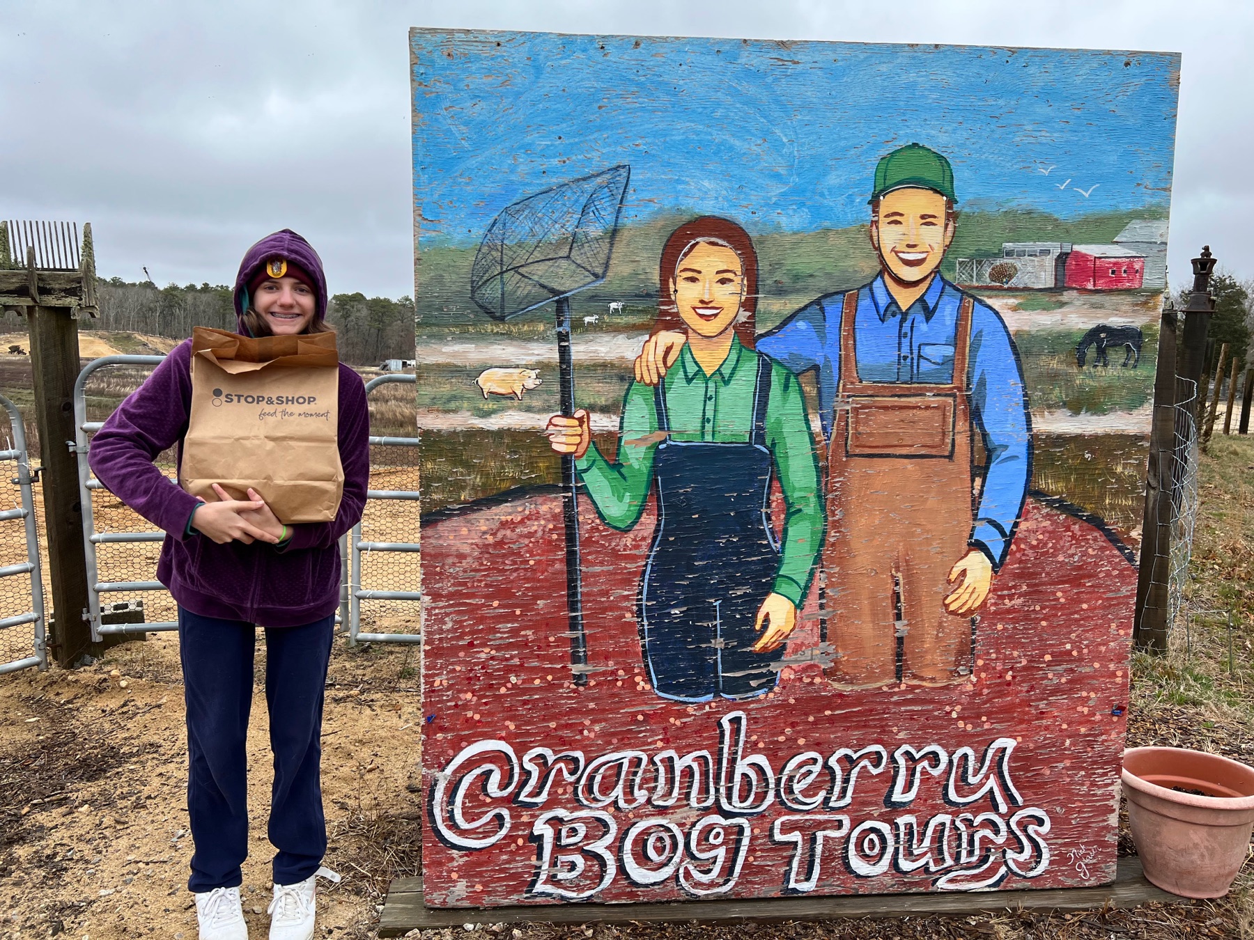 Teenage girl standing beside a painted Cranberry Bog Tours sign in Harwich