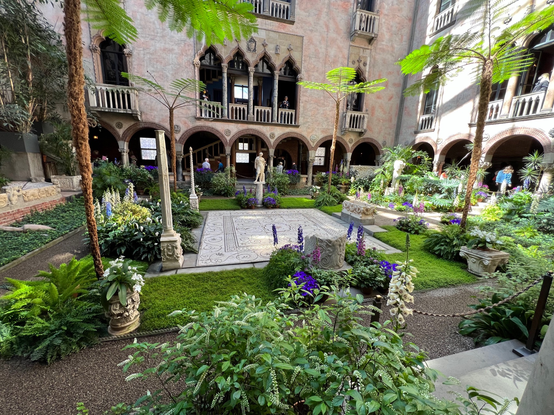 Lush interior courtyard with flowering plants, stone arches, and a fountain at the Isabella Stewart Gardner Museum