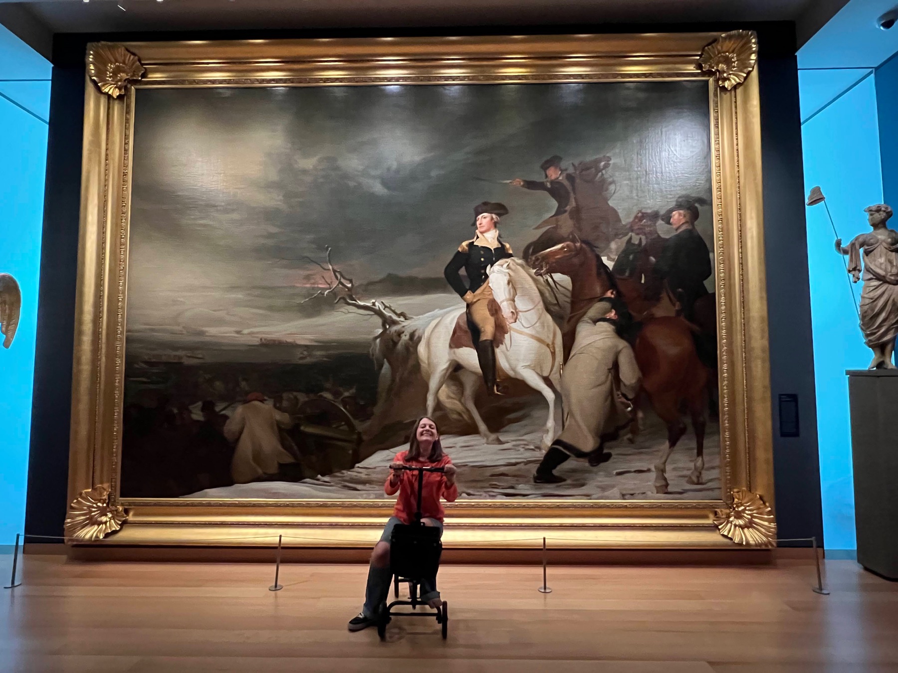 Teenager on a foot scooter seated in front of a large historic painting at the Museum of Fine Arts, Boston