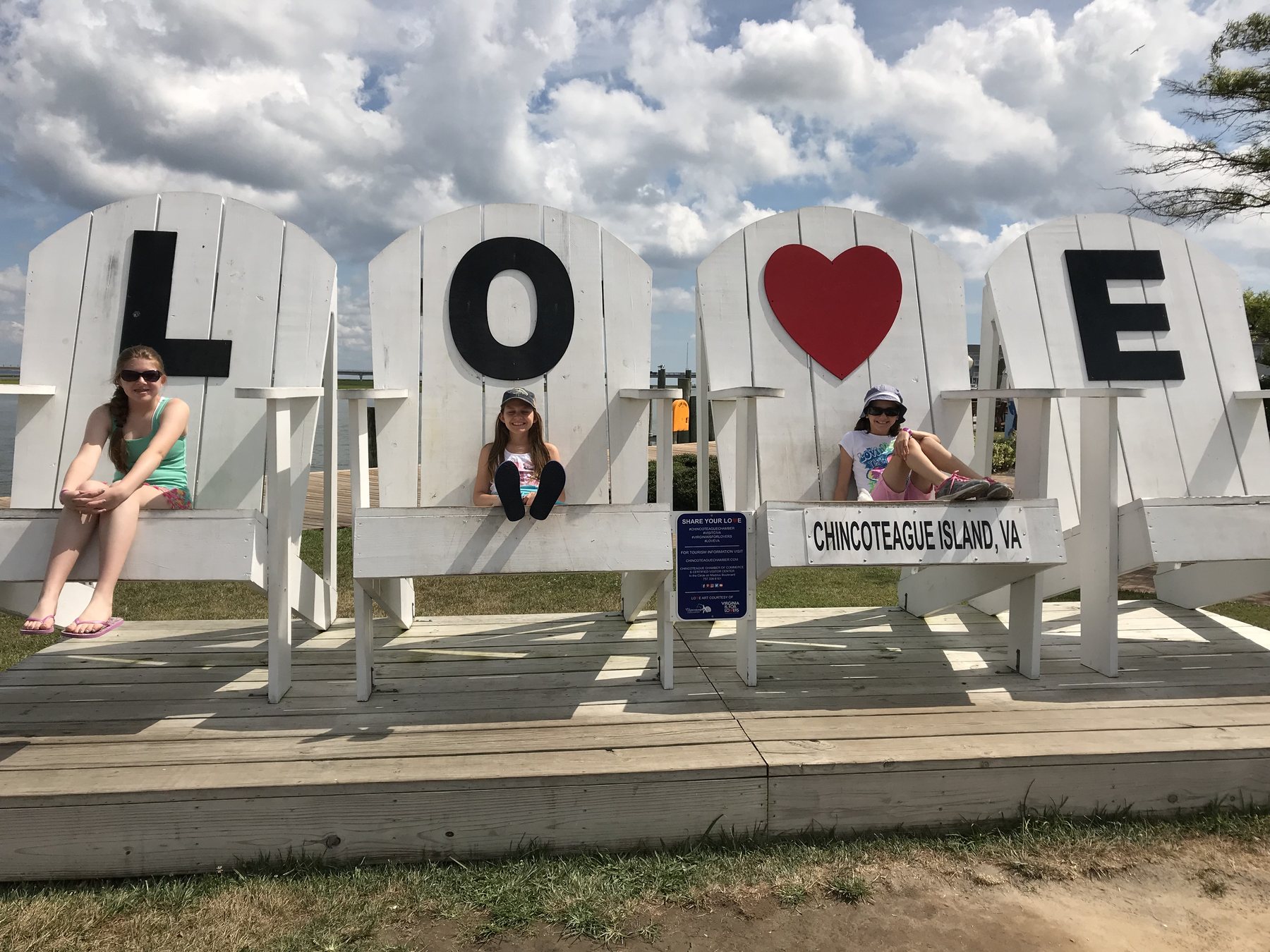 Three children sitting in oversized white chairs spelling LOVE beside the Chincoteague waterfront
