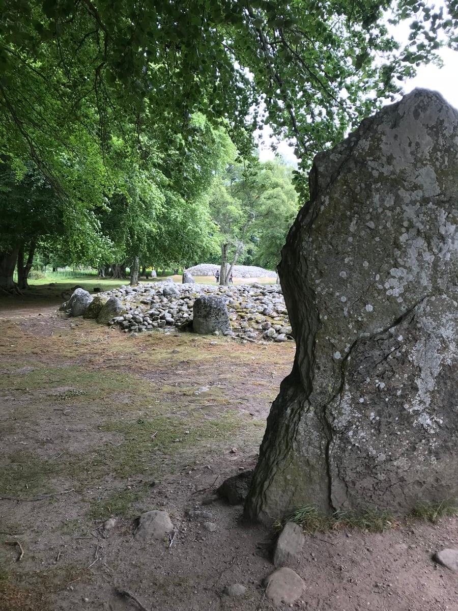 Ancient cairn and standing stones seen through mature trees at Clava Cairns