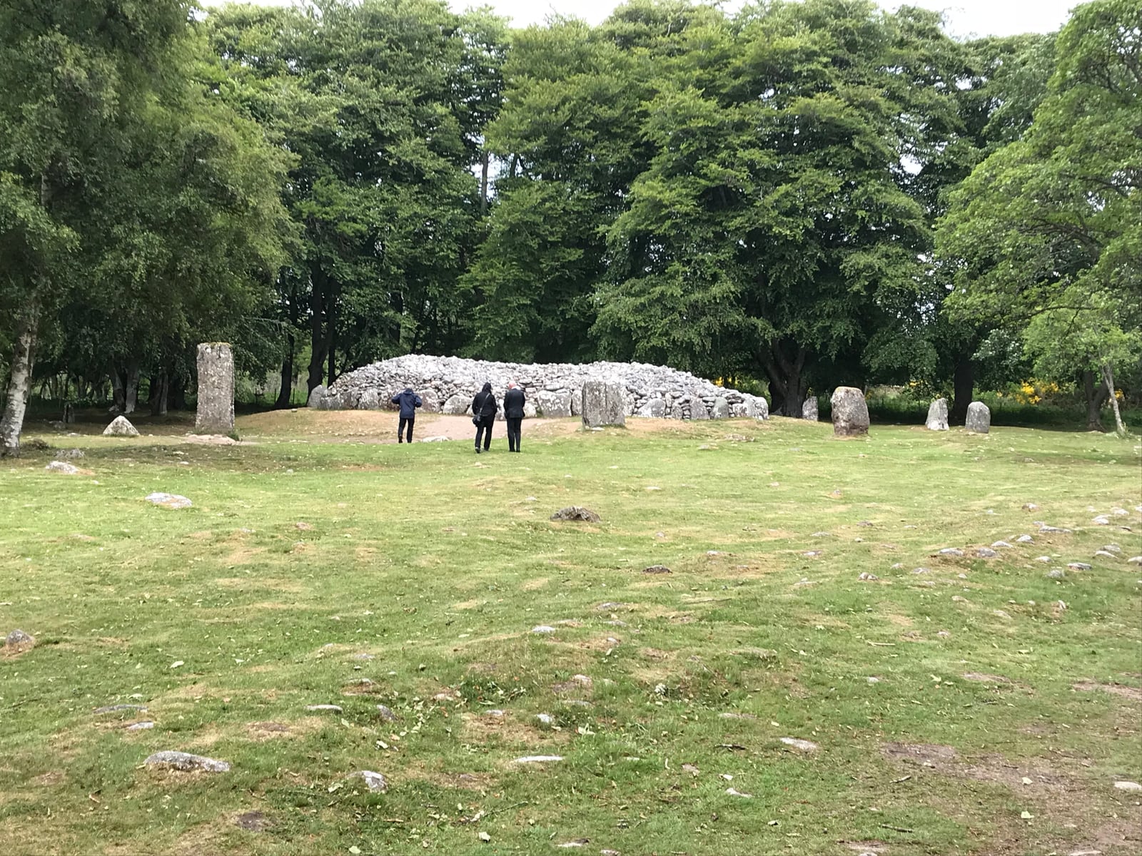 Circular stone cairn and standing stones surrounded by grass and mature trees at Clava Cairns