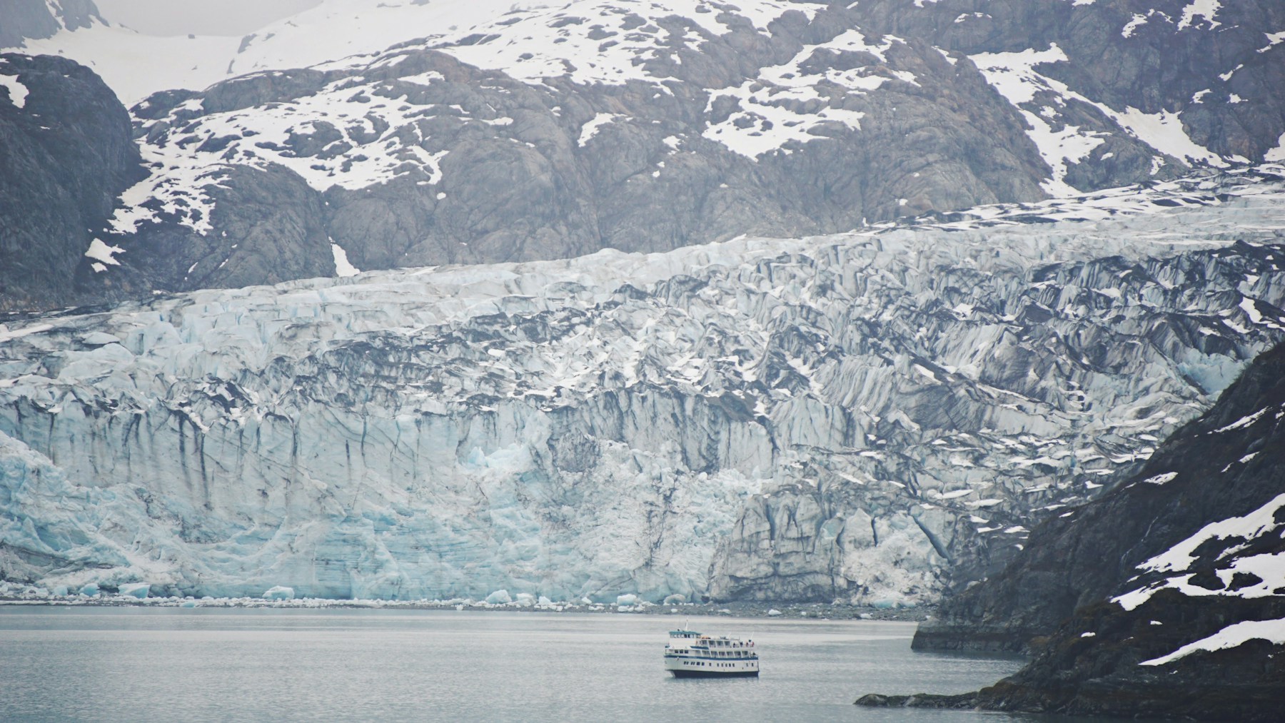 A small cruise vessel on calm water beneath snowy mountains in Glacier Bay, Alaska