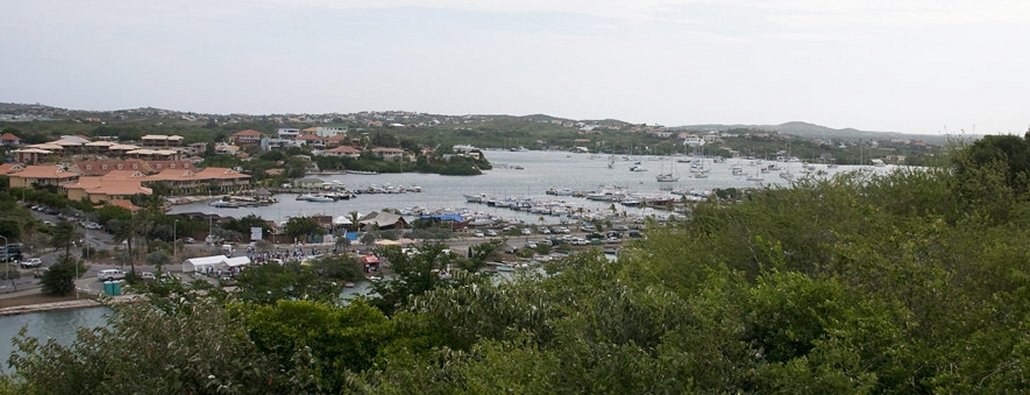Sailboats and yachts at anchor in Spanish Water on Curaçao, with low hills and waterfront buildings behind them