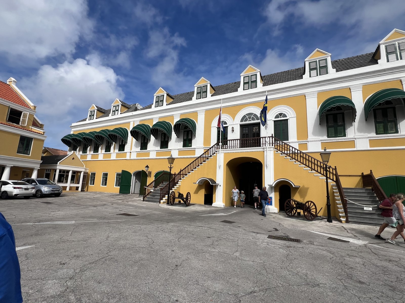 A yellow-and-white historic building with green awnings in downtown Willemstad