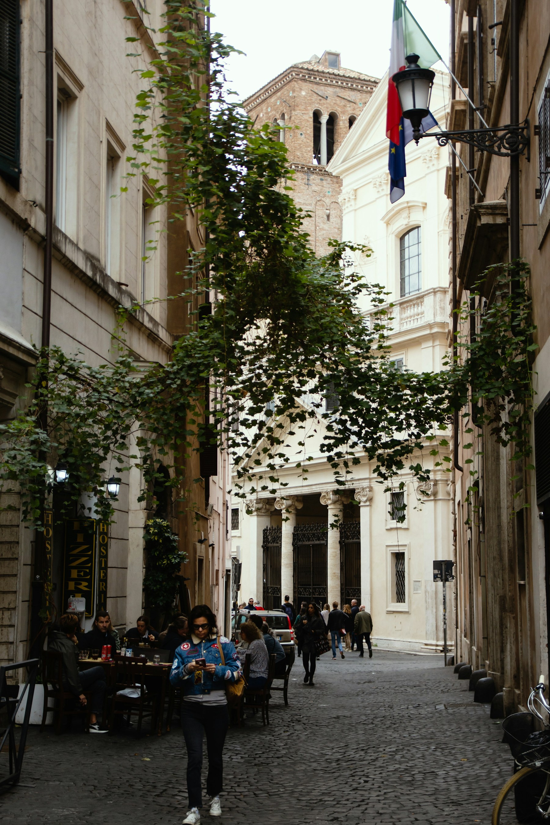 A pedestrian walking along a narrow, plant-lined street in historic Rome