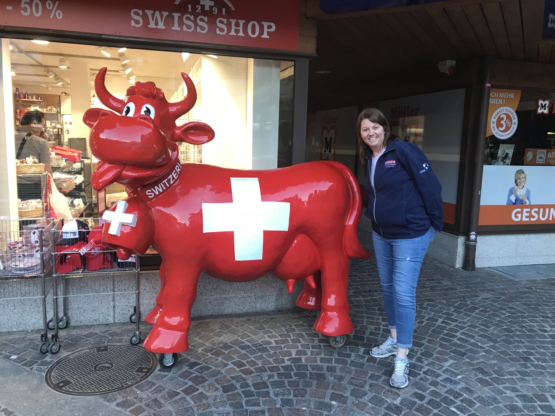 Angela smiling beside a large red Swiss cow figure outside a shop in Zermatt
