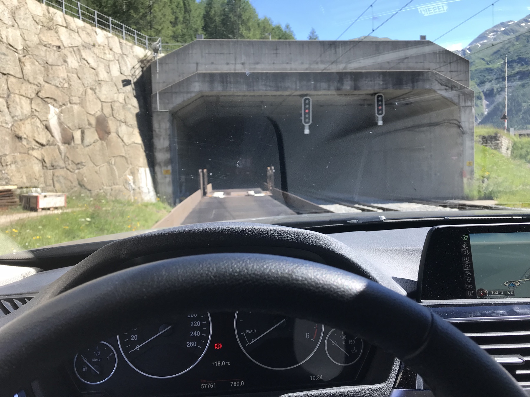 View through a rental-car windshield while approaching the Furka vehicle-shuttle train in Oberwald