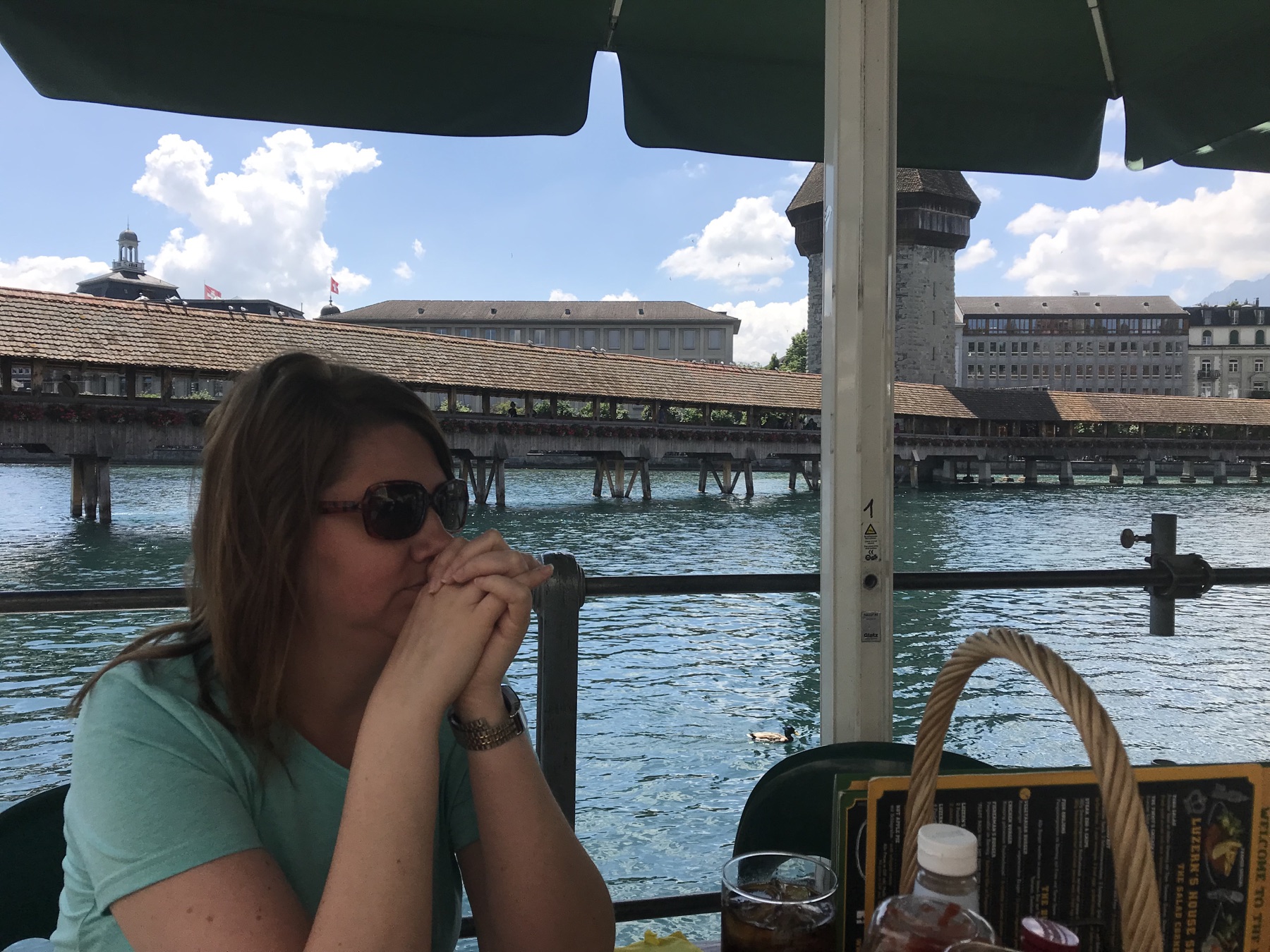 Angela seated at a waterside restaurant with Lucerne's Chapel Bridge behind her
