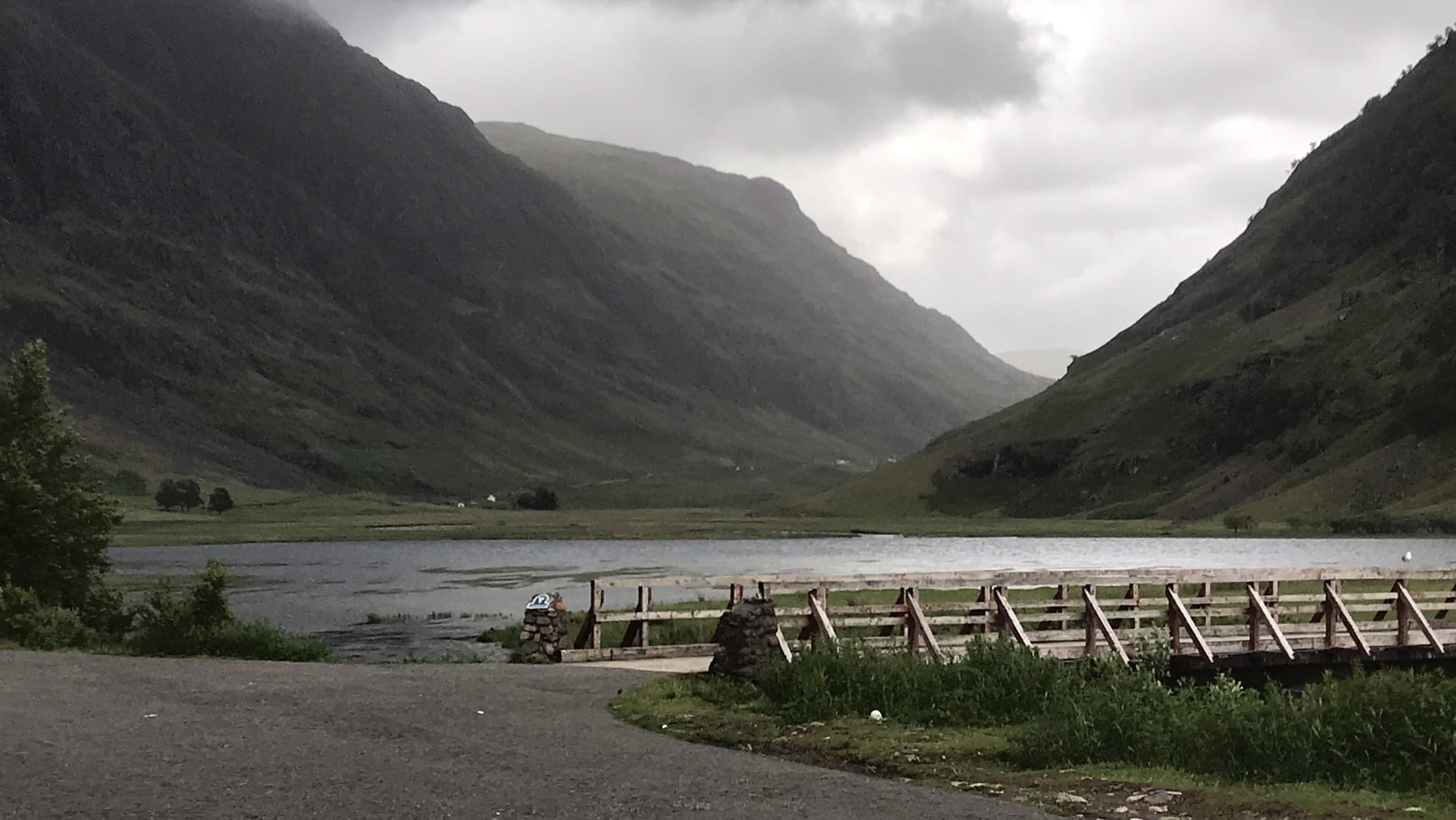 Mountain slopes descending toward water and a wooden walkway in Glencoe