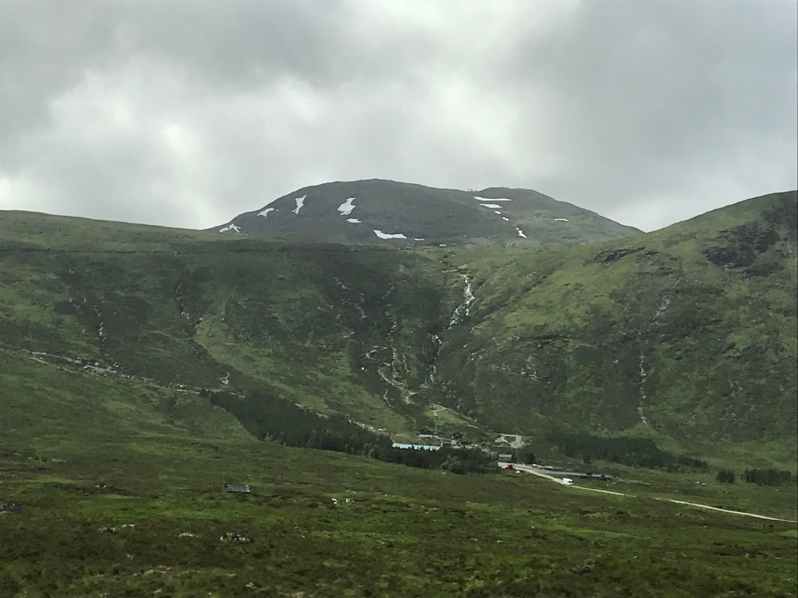 Green Highland mountain slopes with lingering snow and thin waterfalls in Glencoe