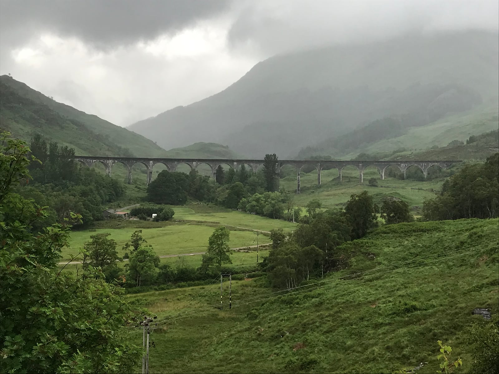 Glenfinnan Viaduct curving across a green Highland valley beneath low gray clouds