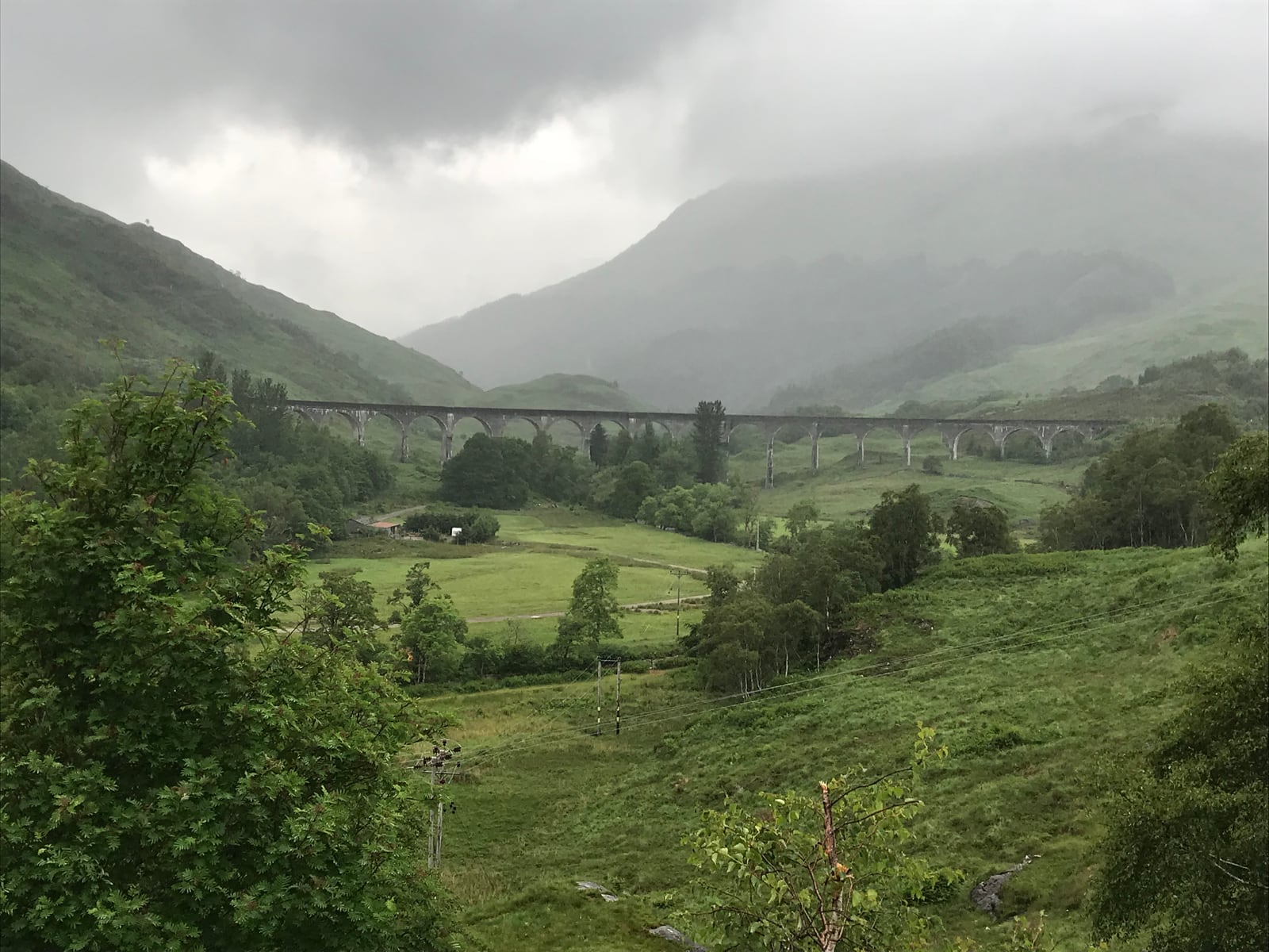 Full curve of Glenfinnan Viaduct crossing the valley beneath mist-covered mountains