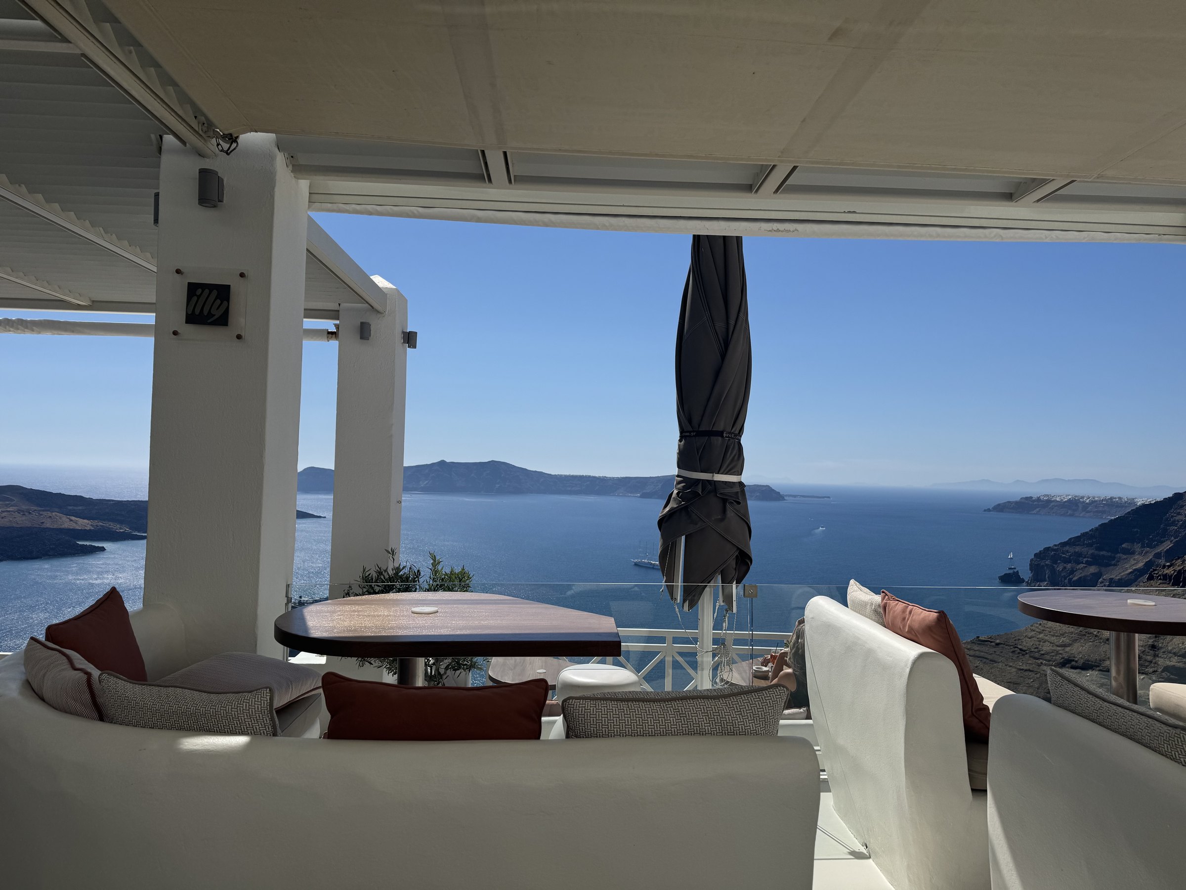 White tables and chairs overlooking the blue caldera from a restaurant terrace in Fira