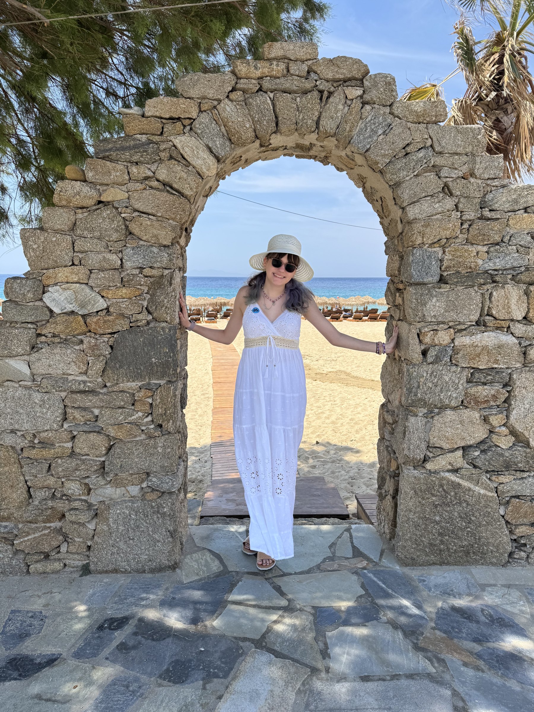 A traveler standing beneath a stone arch with sand and blue water beyond
