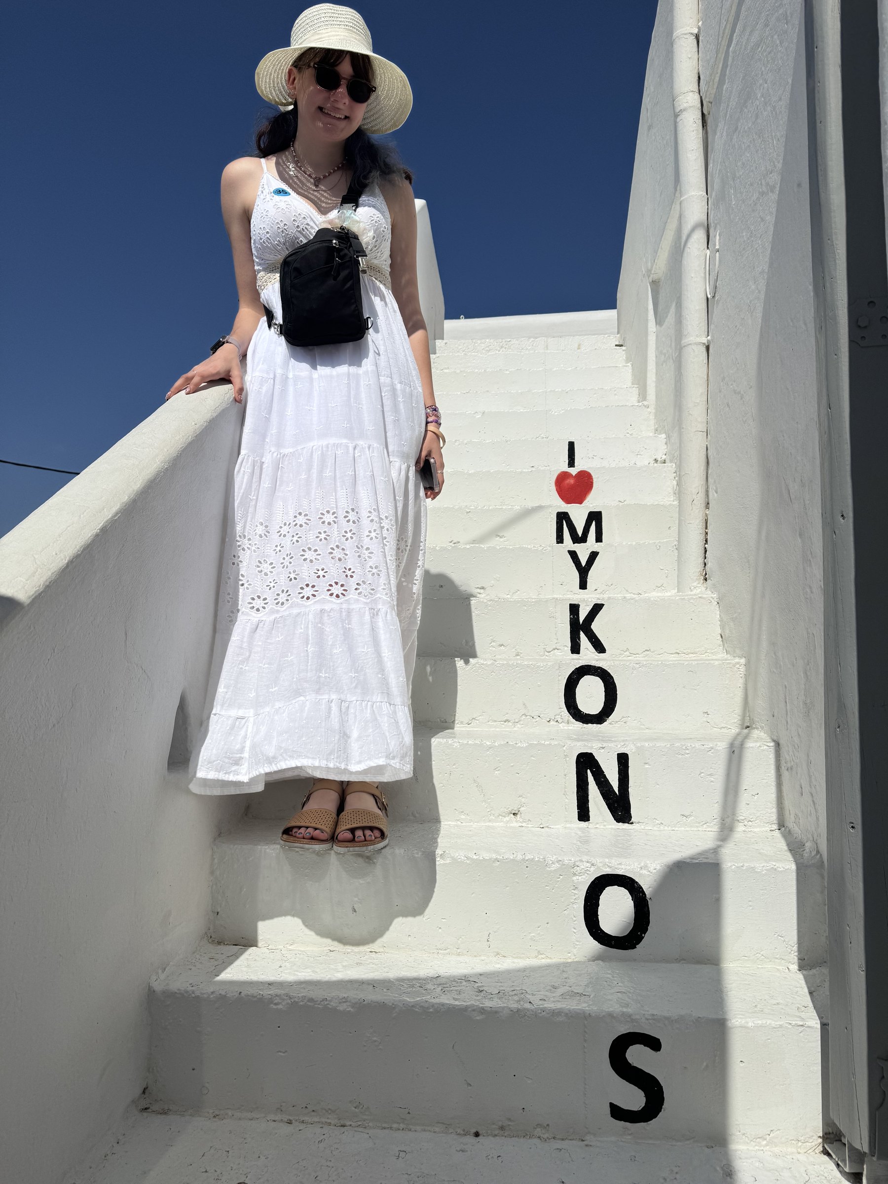 A traveler standing on a narrow whitewashed stairway painted with the word Mykonos