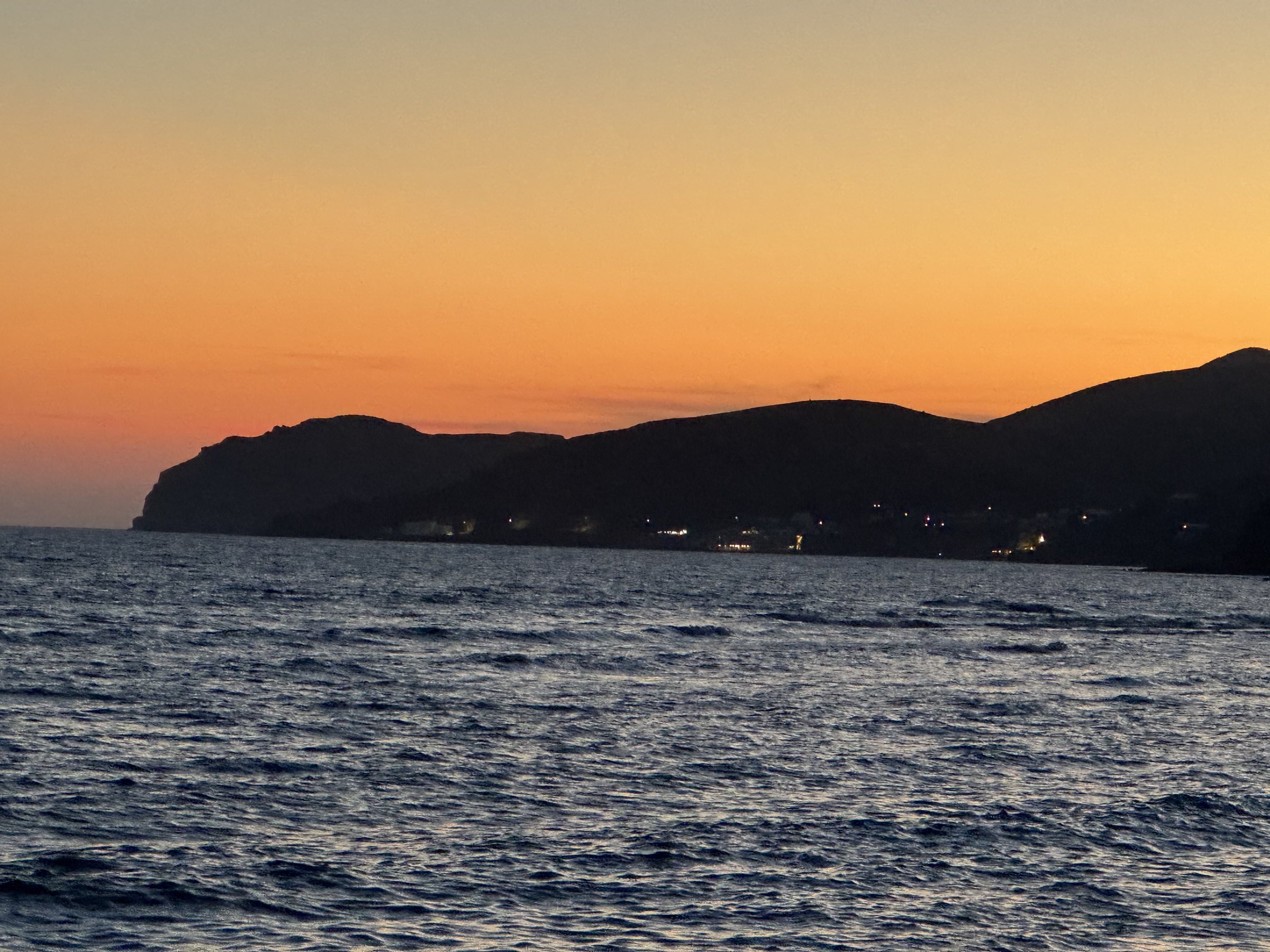 Orange sunset sky above the dark silhouette of the Santorini coast and the Aegean Sea