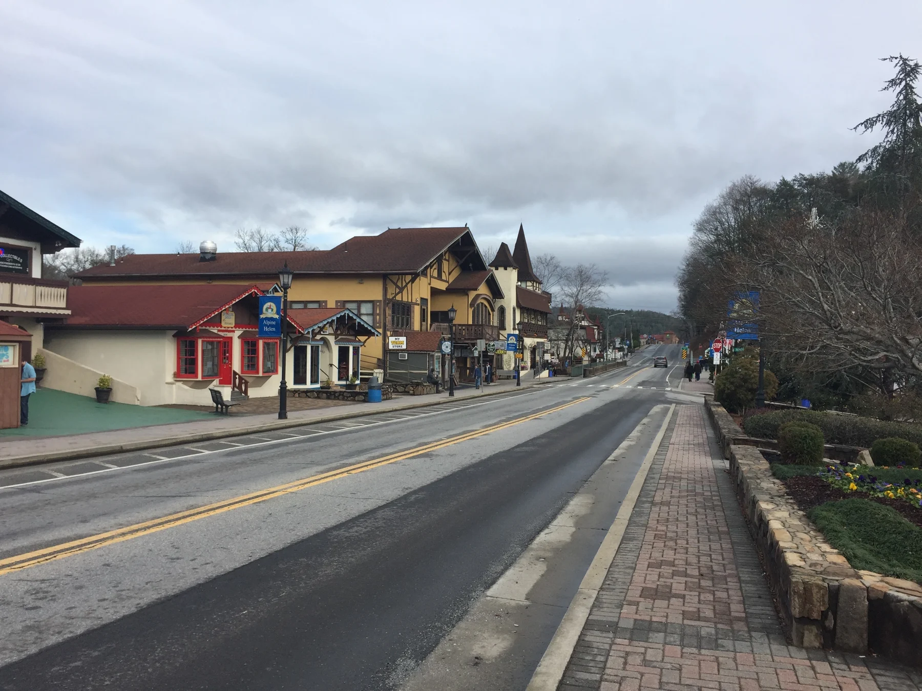 A sidewalk beside the main road through Helen, lined with Alpine-style shops under cloudy skies