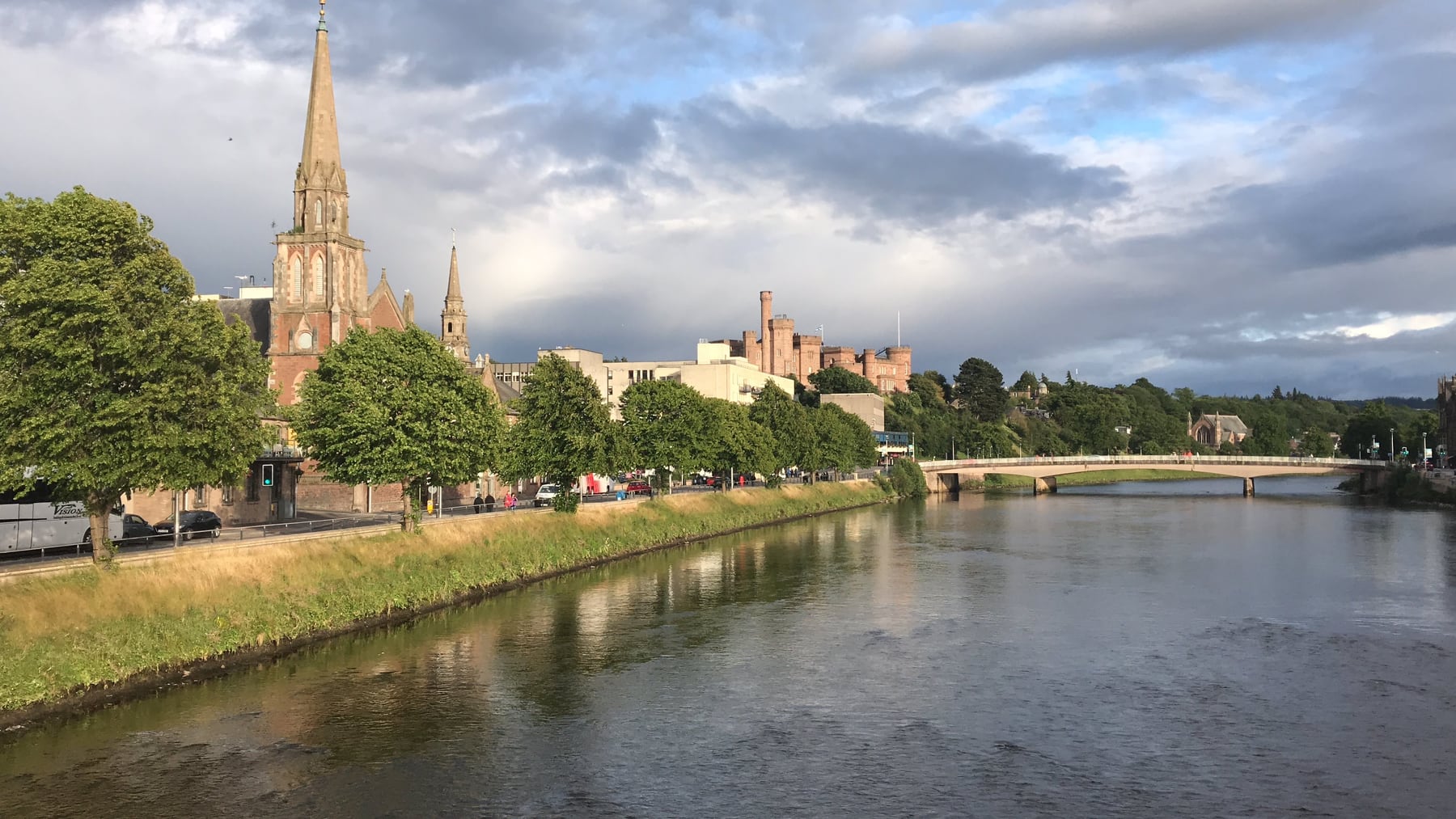 River Ness flowing through Inverness with church spires and Inverness Castle beneath a dramatic sky
