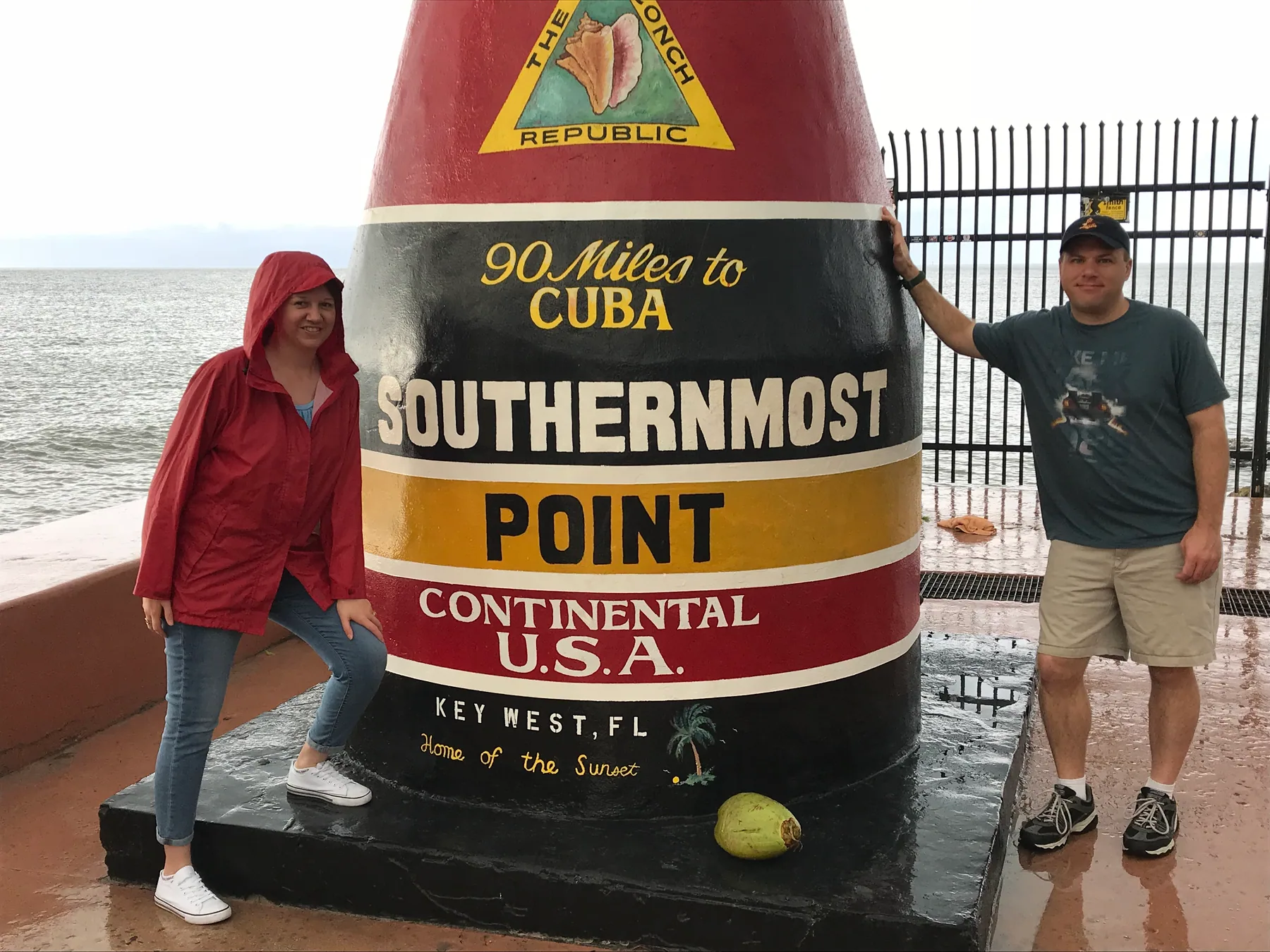Angela and Brian in rain jackets beside the Southernmost Point marker in Key West