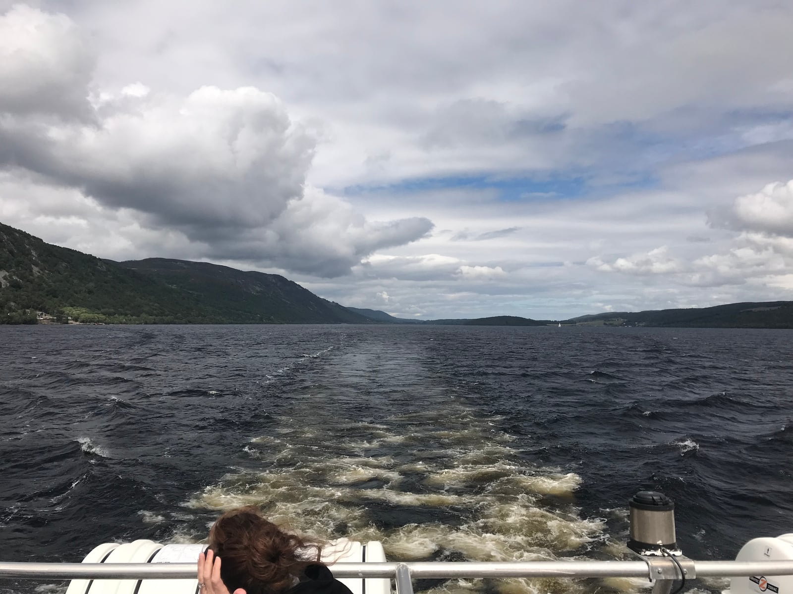 Boat wake stretching across the dark water of Loch Ness between green Highland slopes