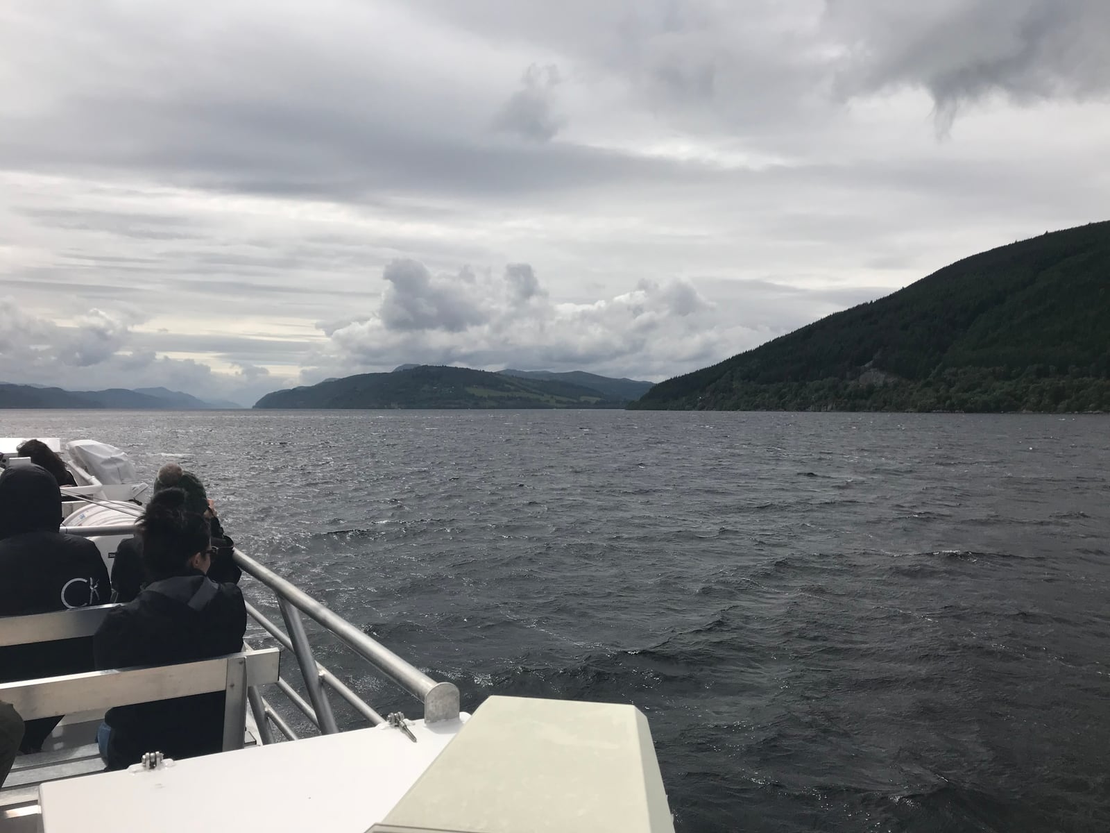 Passengers looking across Loch Ness from the open deck of a cruise boat