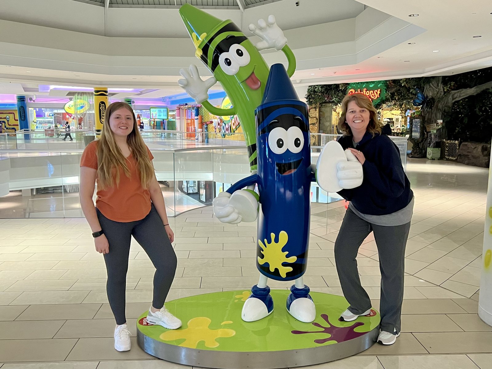 Angela and Madison standing beside large Crayola crayon characters inside Mall of America