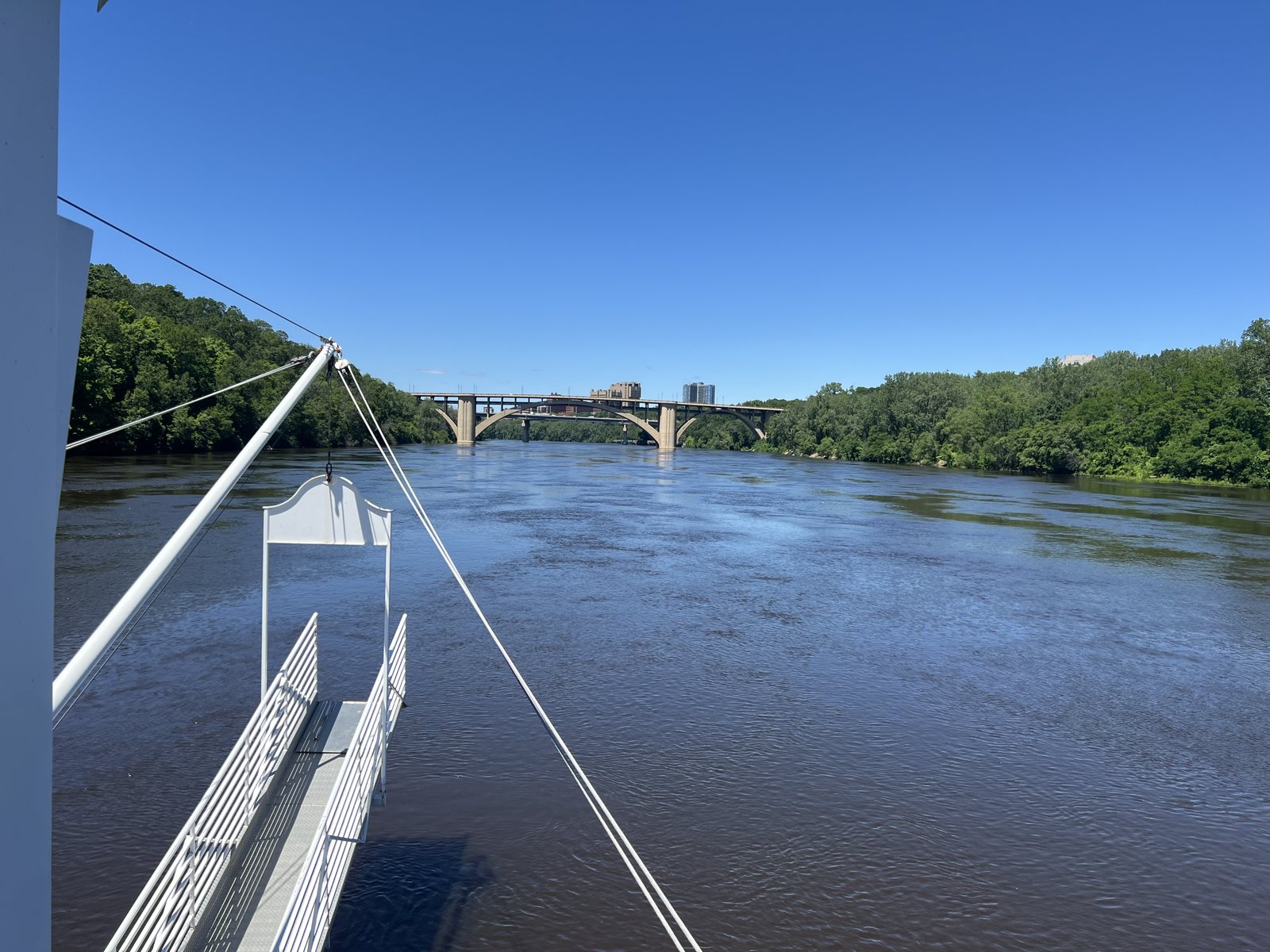 The Mississippi River stretching toward a low arch bridge and the tree-lined Minneapolis riverbank