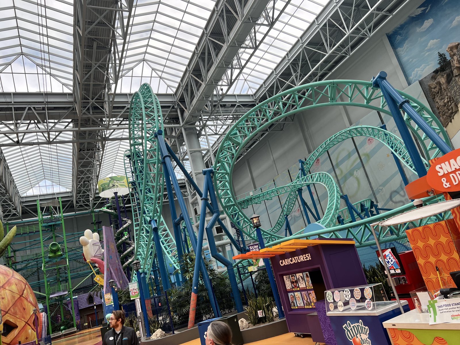 A green indoor roller coaster twisting under the glass roof of Nickelodeon Universe