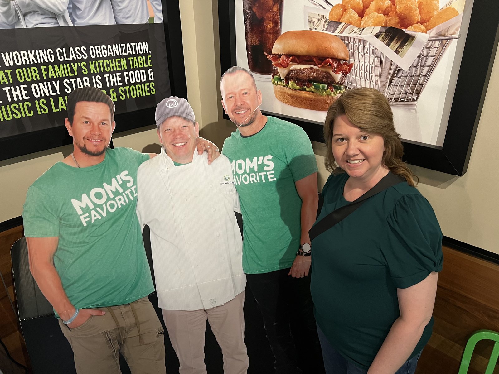 Angela smiling beside cardboard cutouts of the Wahlberg brothers at Wahlburgers