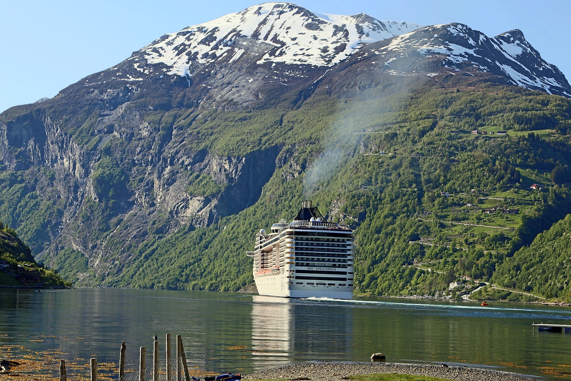 A cruise ship sailing through Geirangerfjord below snow-covered mountains in Norway
